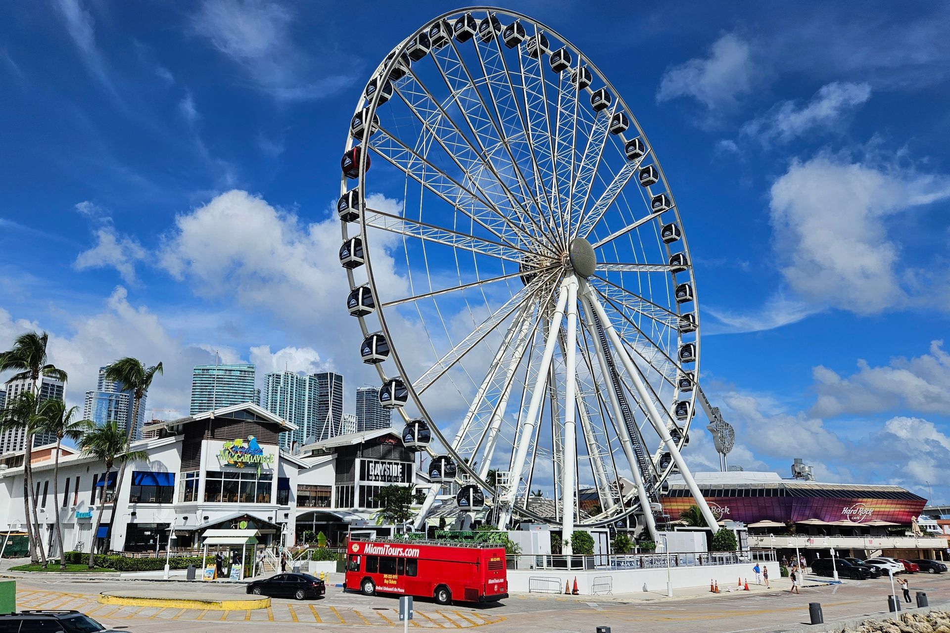 Ferris wheel and buildings on waterfront under blue sky with clouds. Red tour bus.