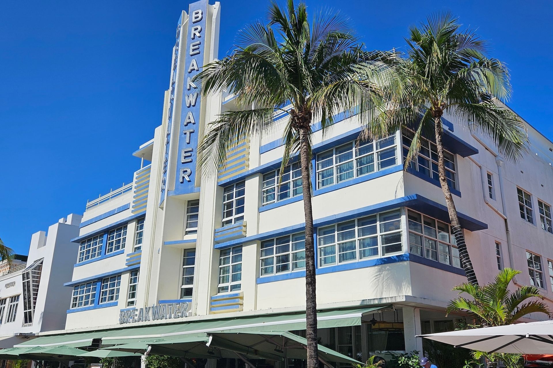 Oceanfront hotel in Miami, Art Deco style, white and blue facade, palm trees, sunny day.