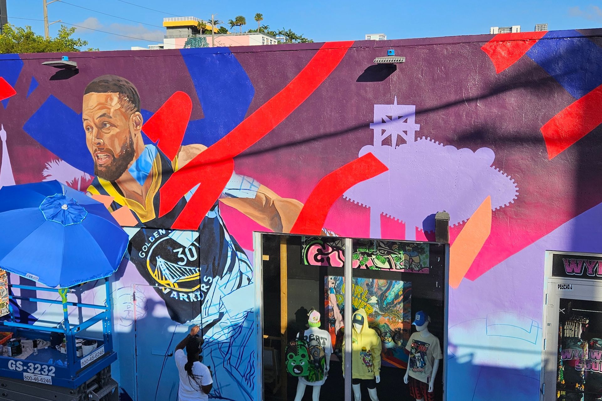 Mural of Stephen Curry on a building exterior, with a shop entrance, featuring bright colors.