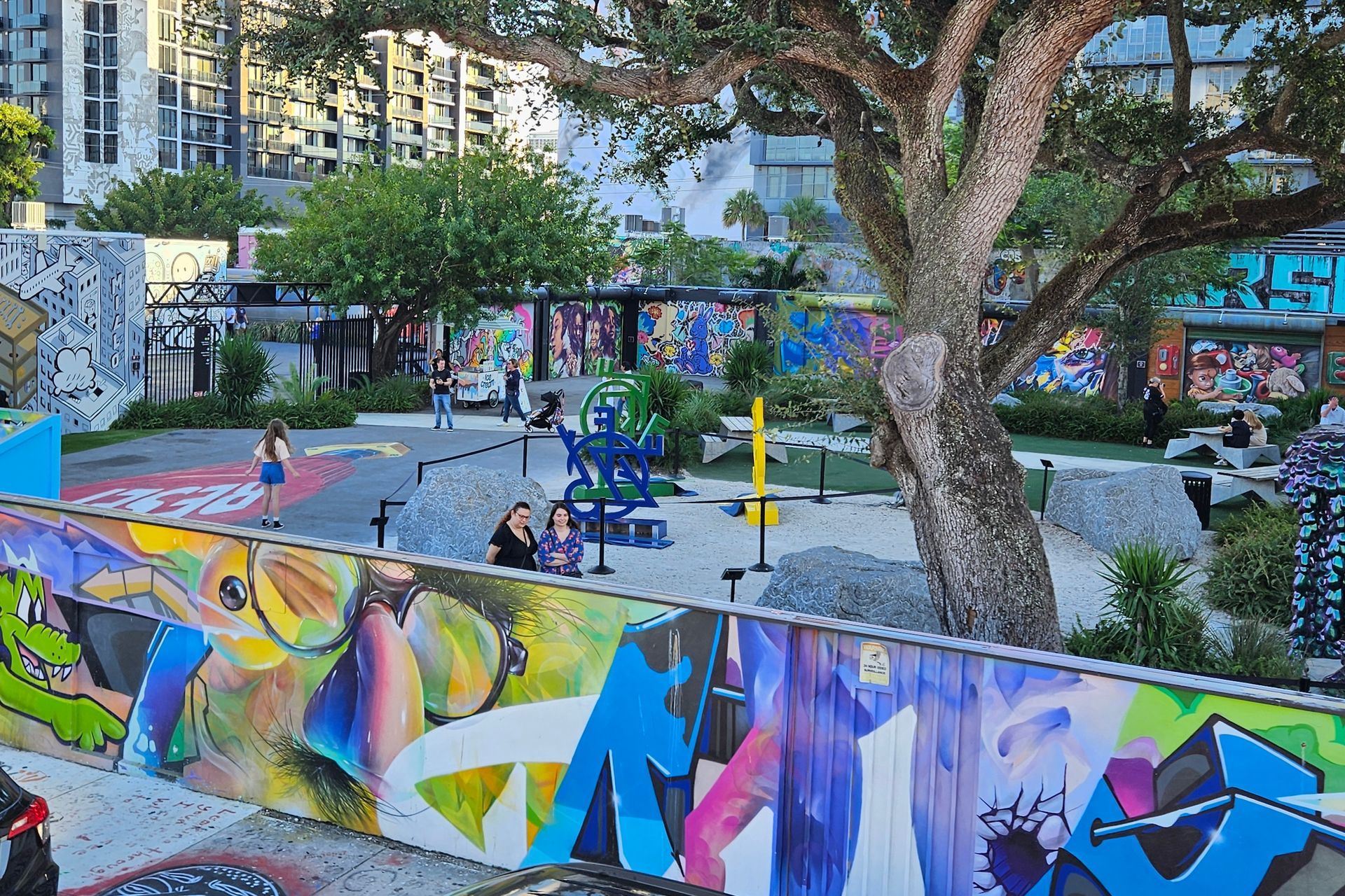 Colorful graffiti art on walls surrounds a park with a playground, people, and trees.