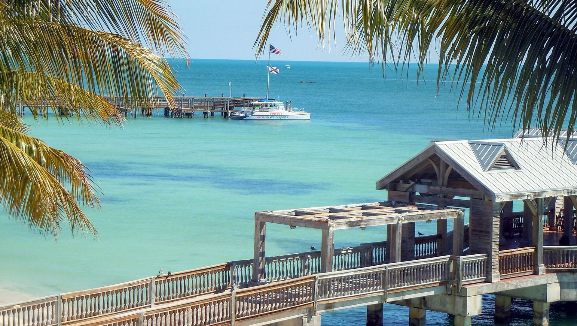Pier stretching over turquoise water in Key West, Florida, with a boat and palm trees.
