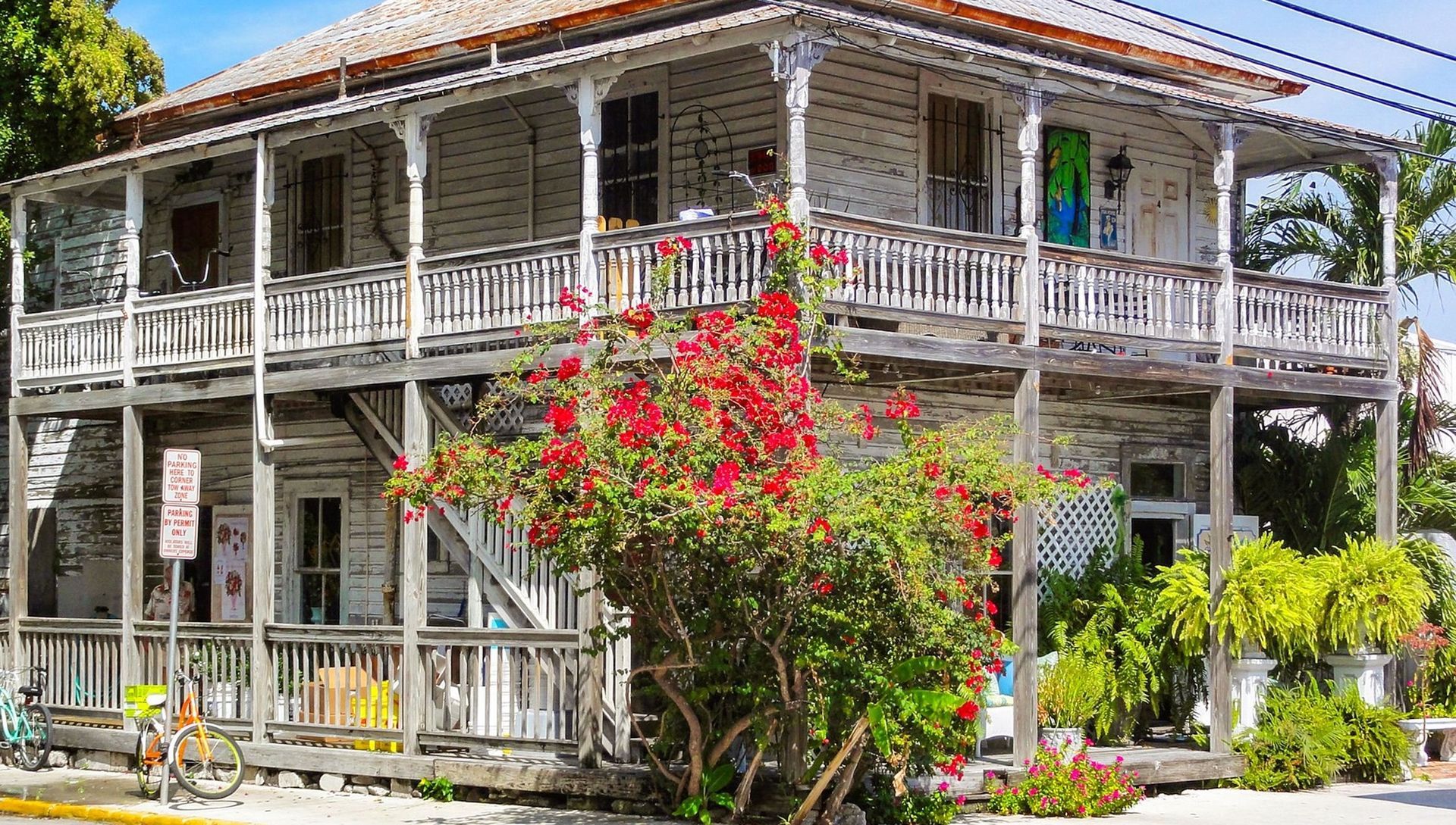 Two-story white wooden house with a porch and blooming red flowers in Key West.