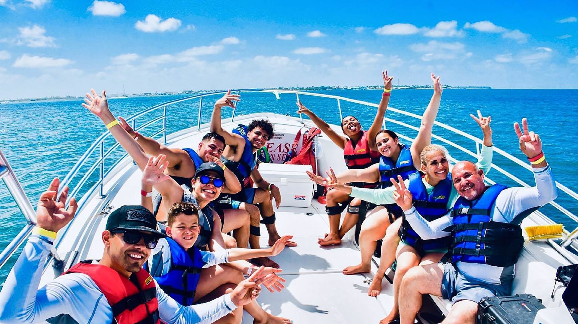 Group of people on a boat, waving and smiling under a sunny sky.