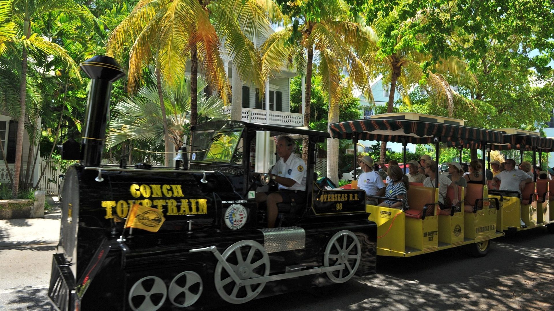 A black and yellow Conch Tour Train on a street with tourists and palm trees in Key West.