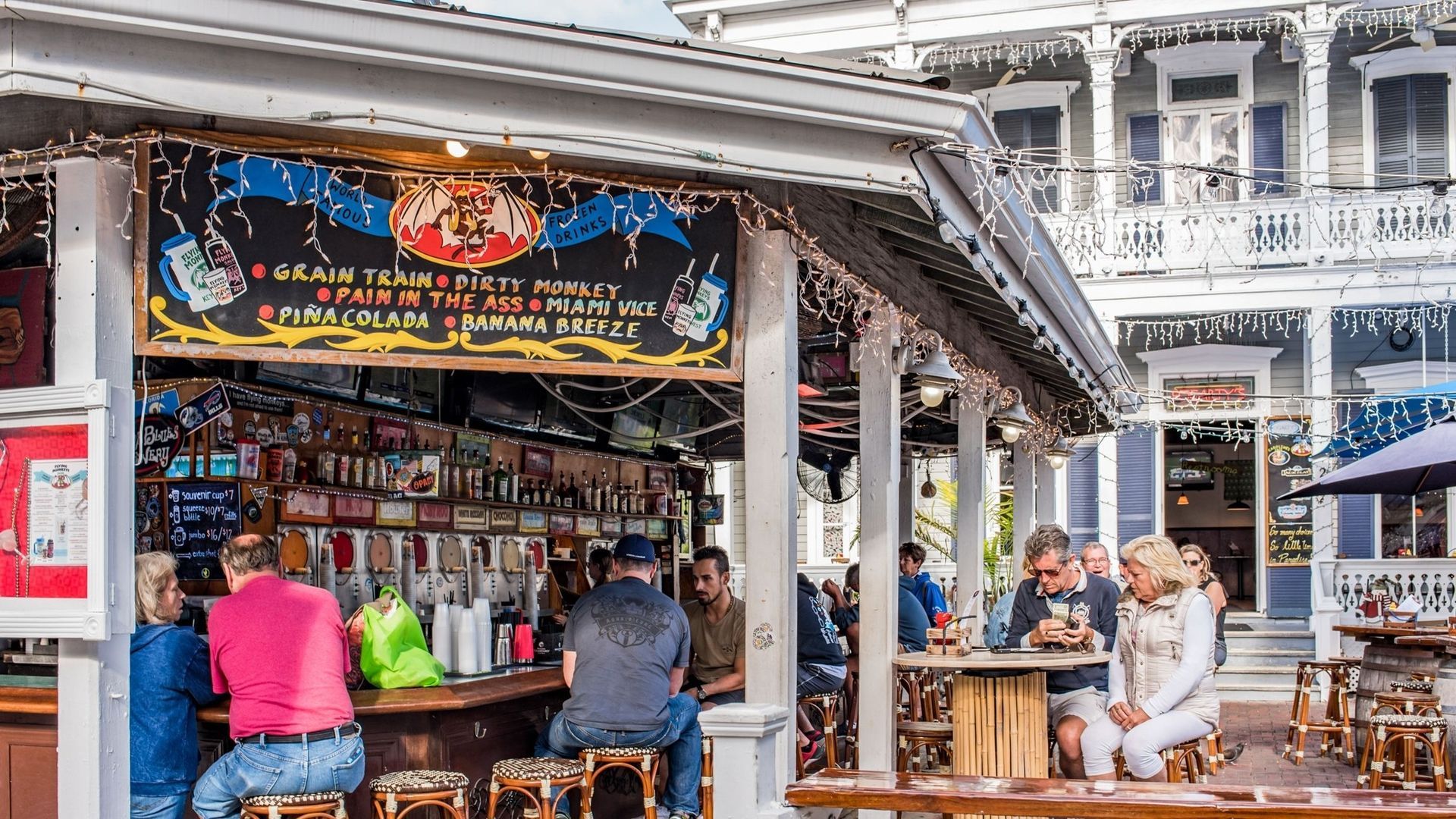Outdoor bar with people, sign, and historic building in the background.