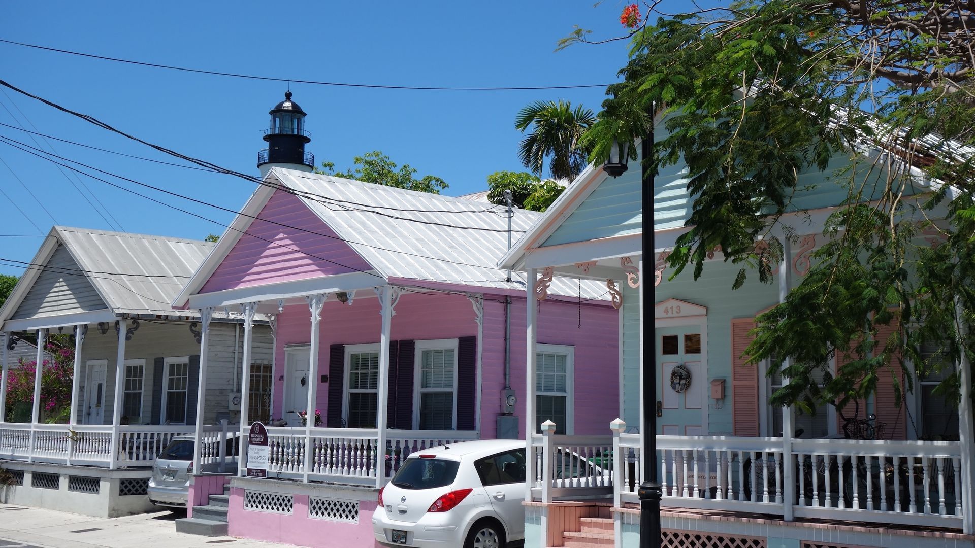 Row of colorful pastel houses under a bright blue sky; white car parked in front.