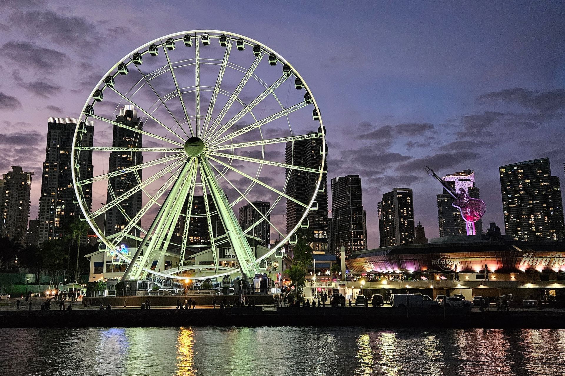 Ferris wheel lit at dusk with city skyline in the background.