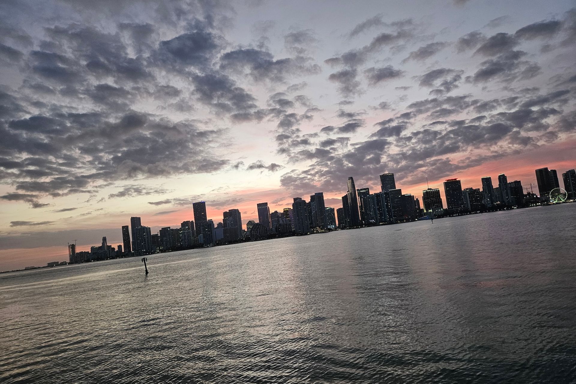 Skyline silhouette at sunset over water; pink and grey clouds.