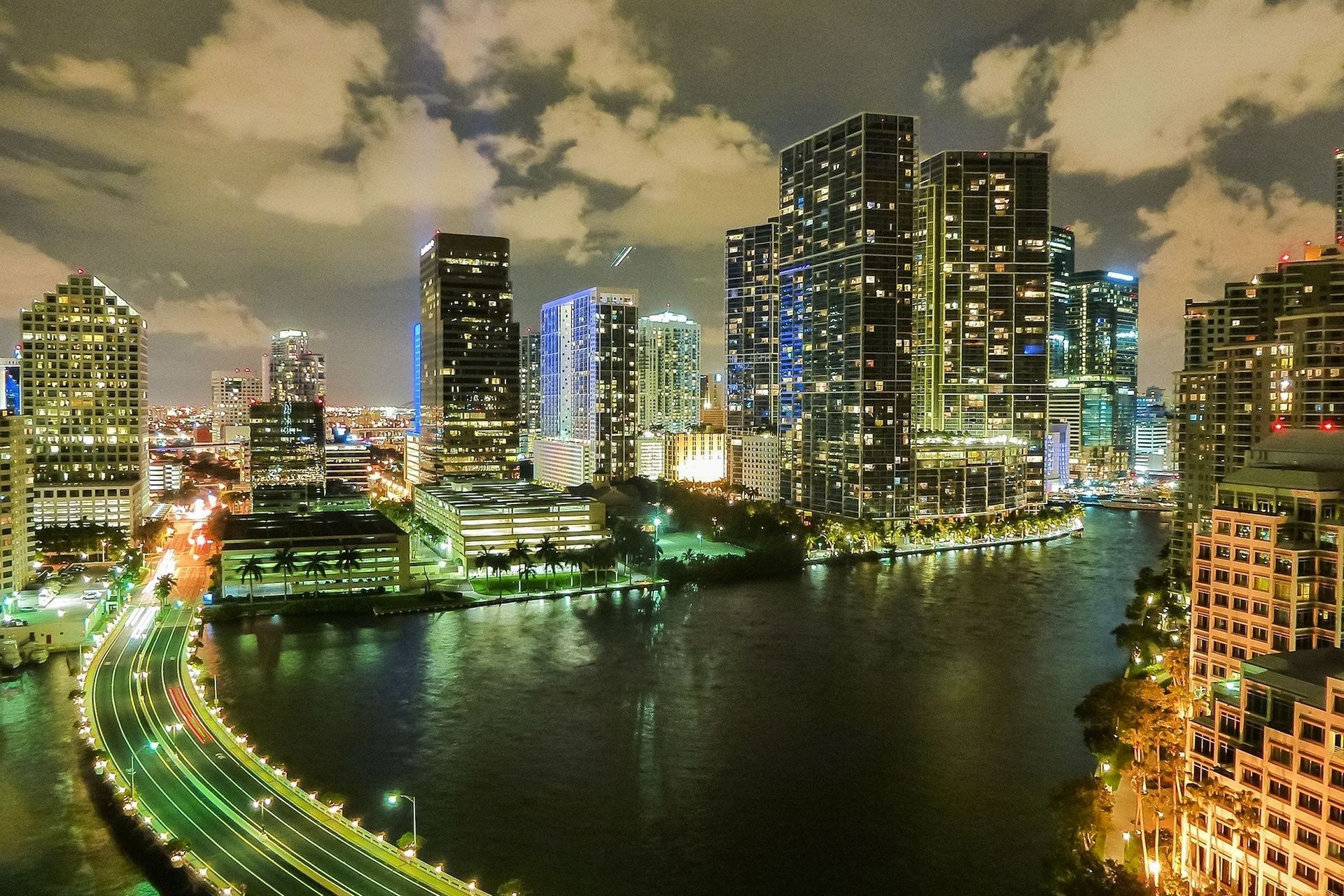 Miami skyline at night, illuminated skyscrapers reflecting in the dark water.