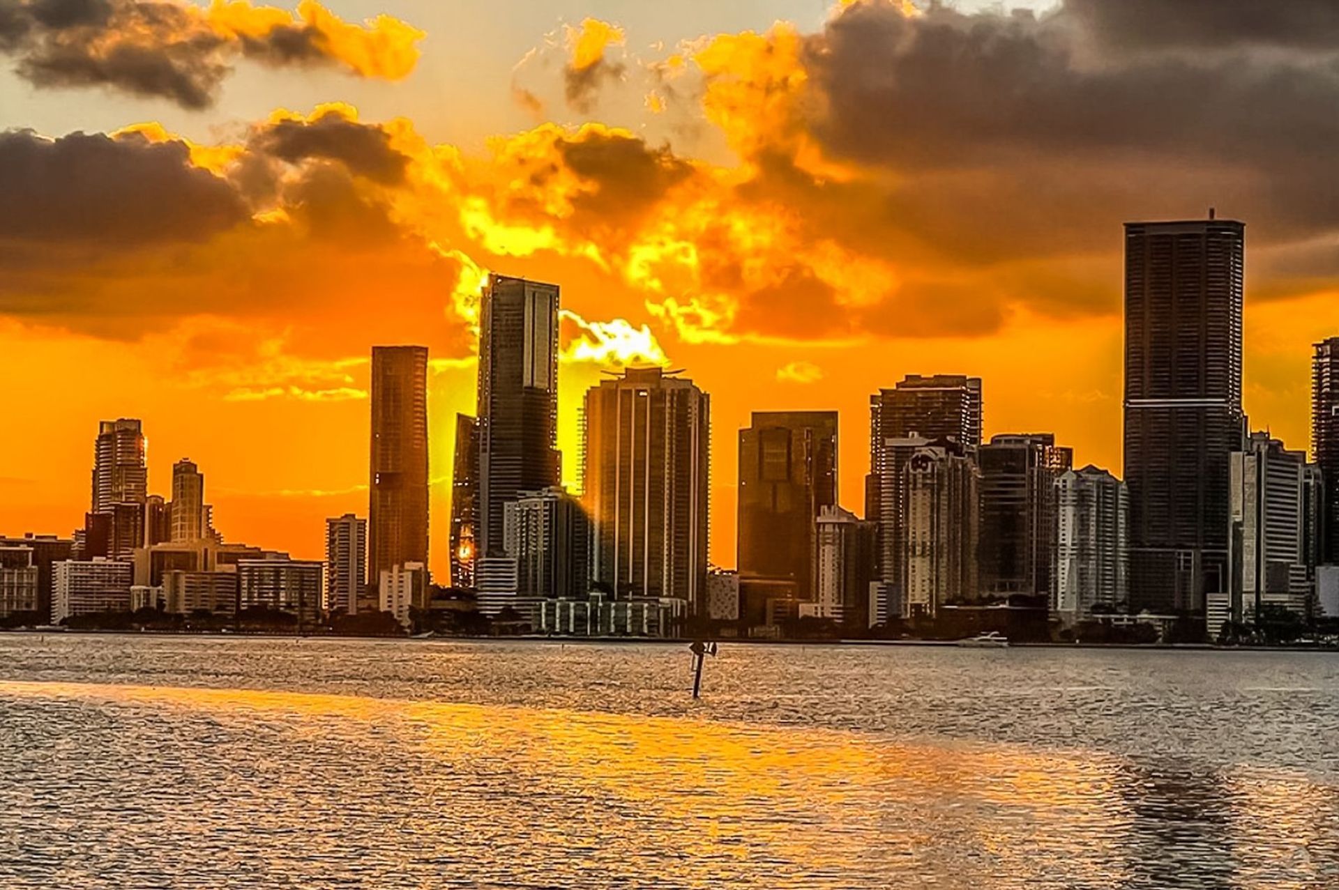 Miami skyline silhouetted against a golden sunset, reflecting on water.