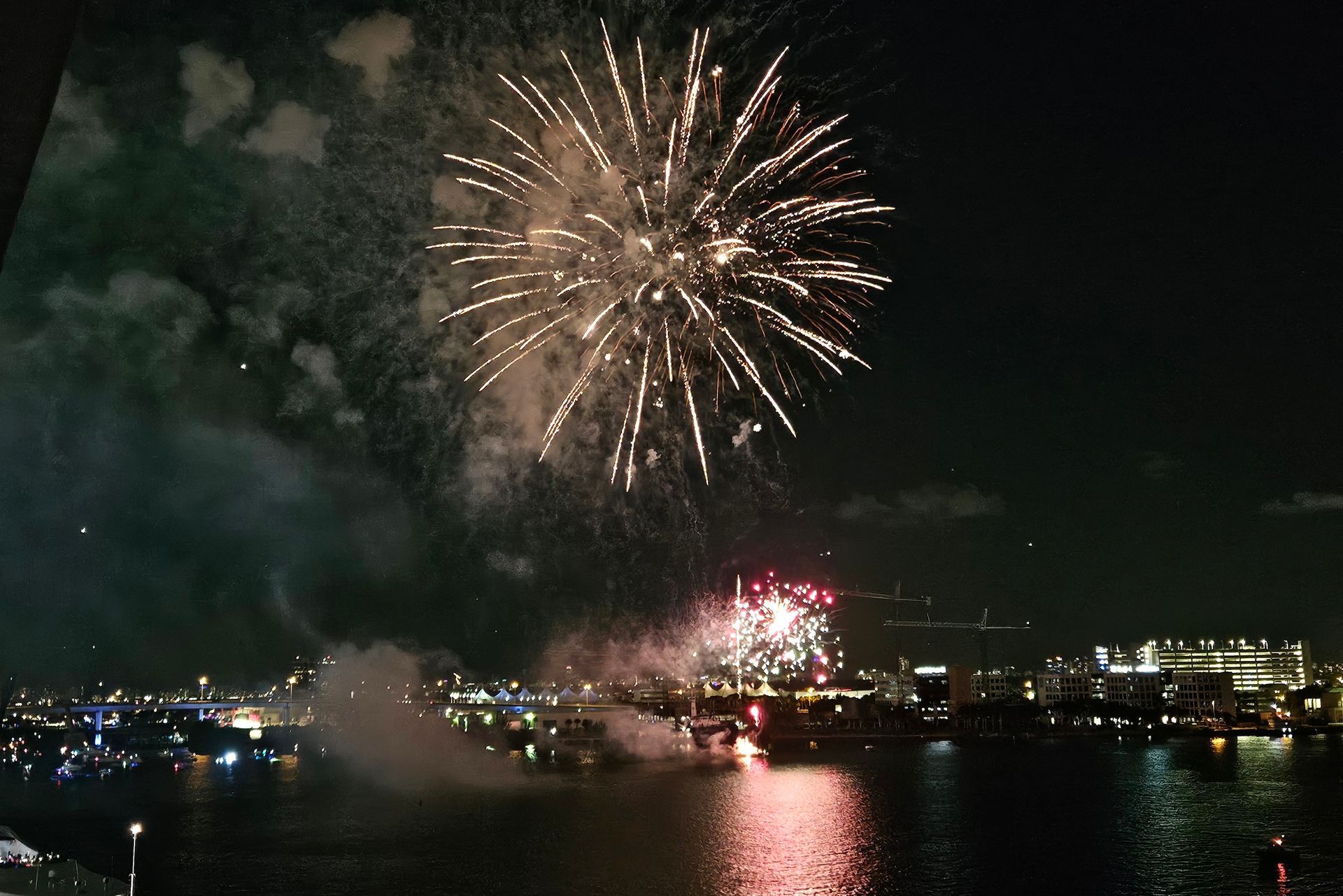 Fireworks exploding over a dark body of water and city skyline at night.