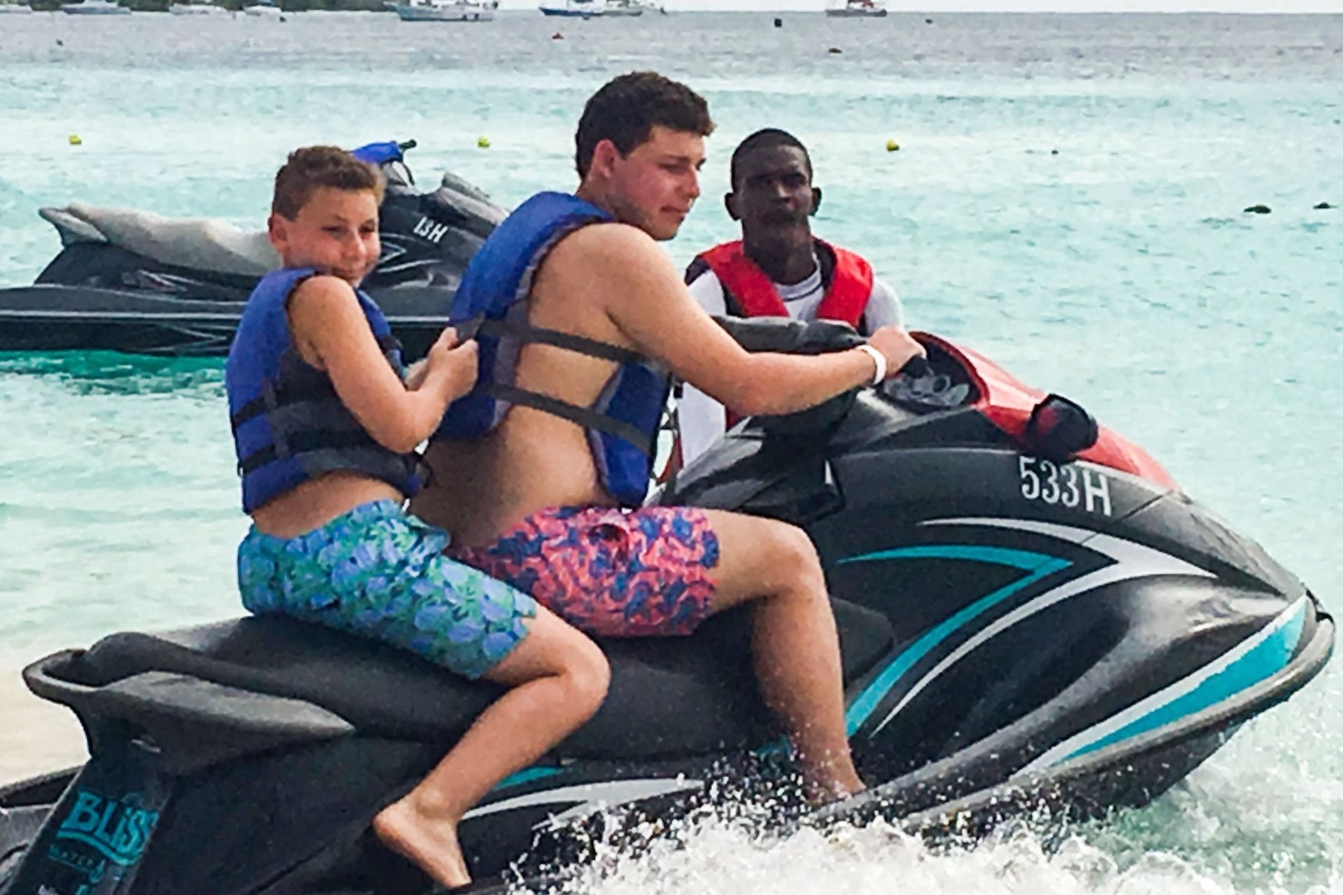 Man and boy on a jet ski, another man on the back, by the beach.