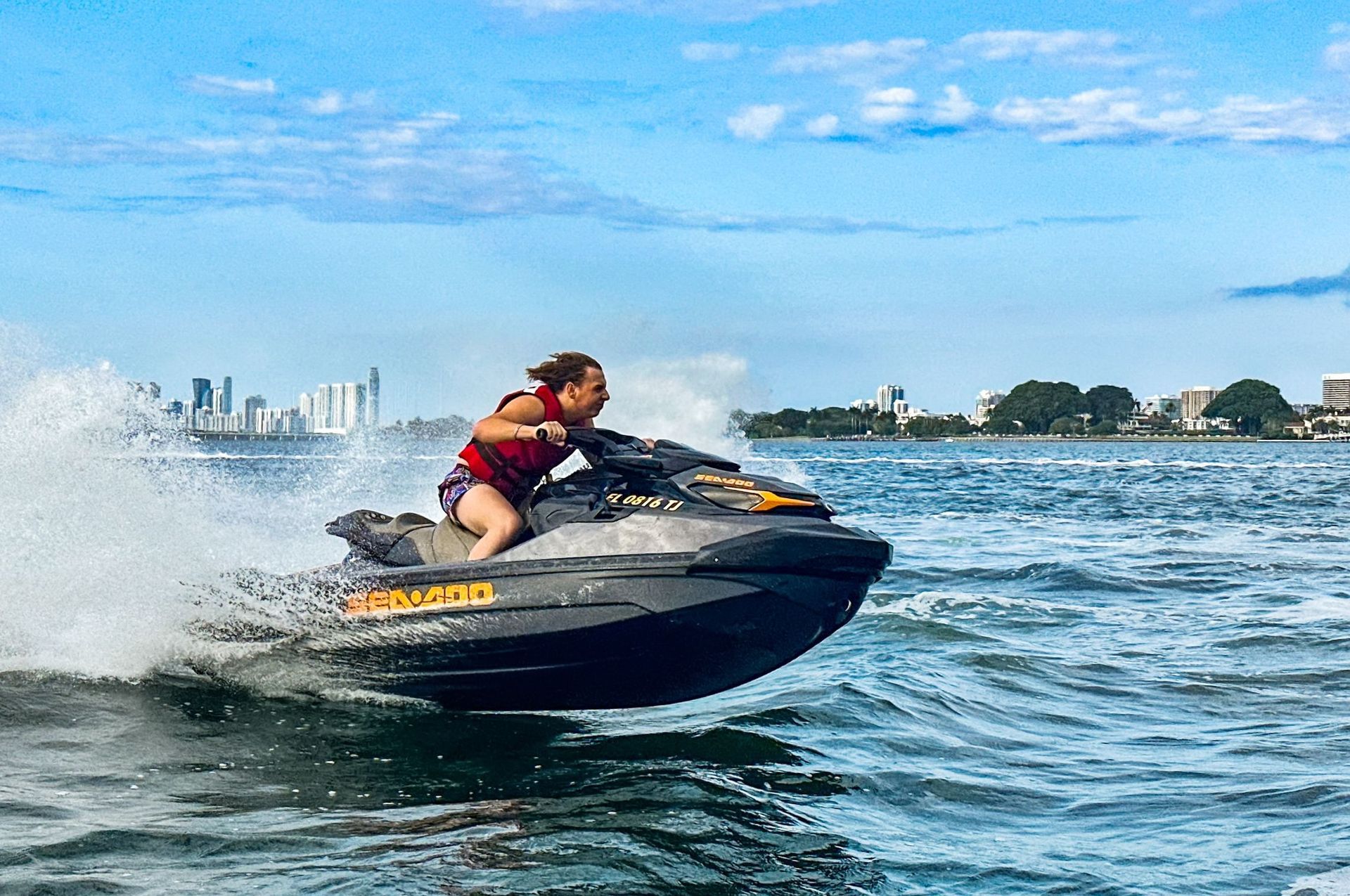 Person riding a jet ski on water, with city skyline in the background.