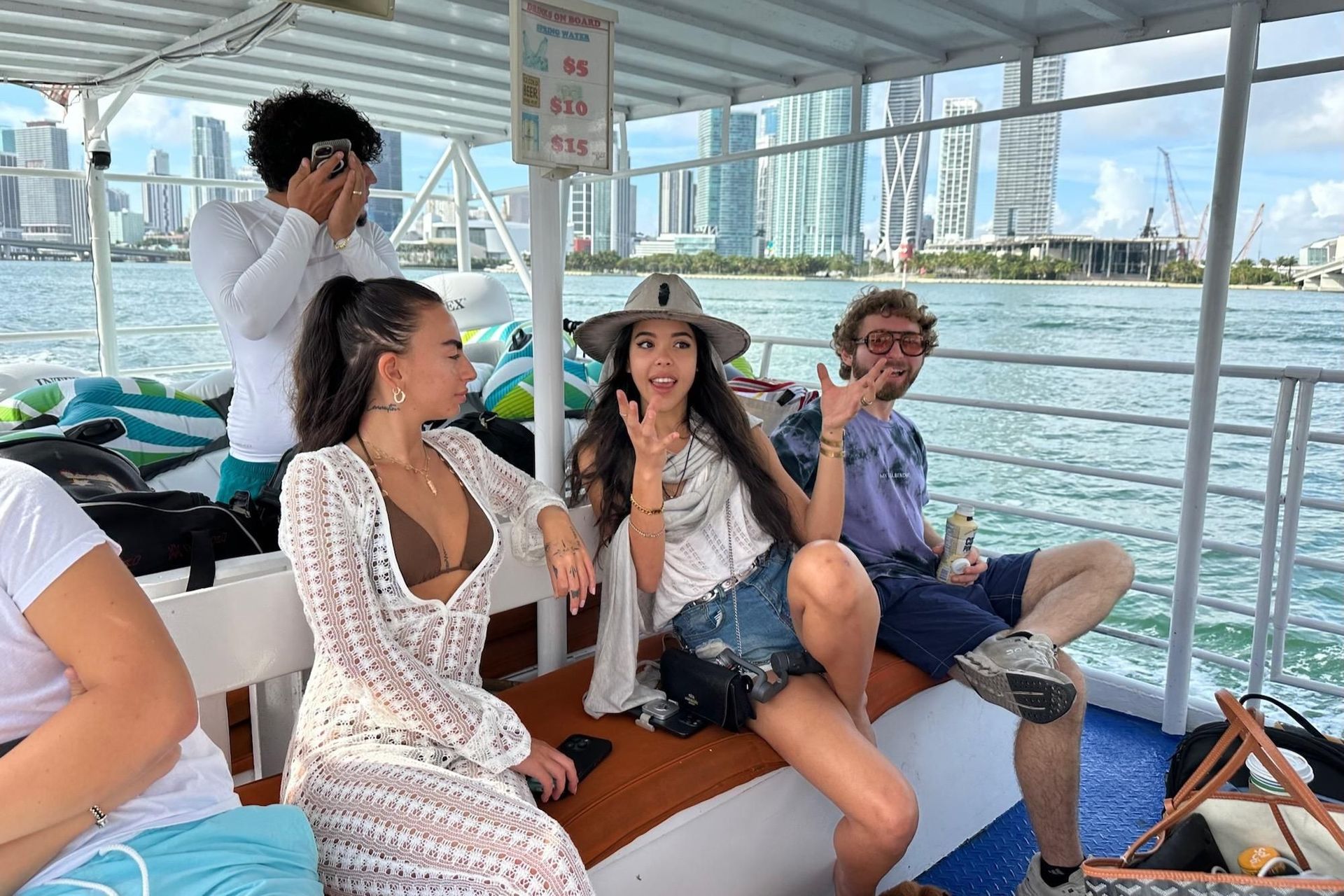 People on a boat in Miami, one pointing with excitement. Tall buildings in background.