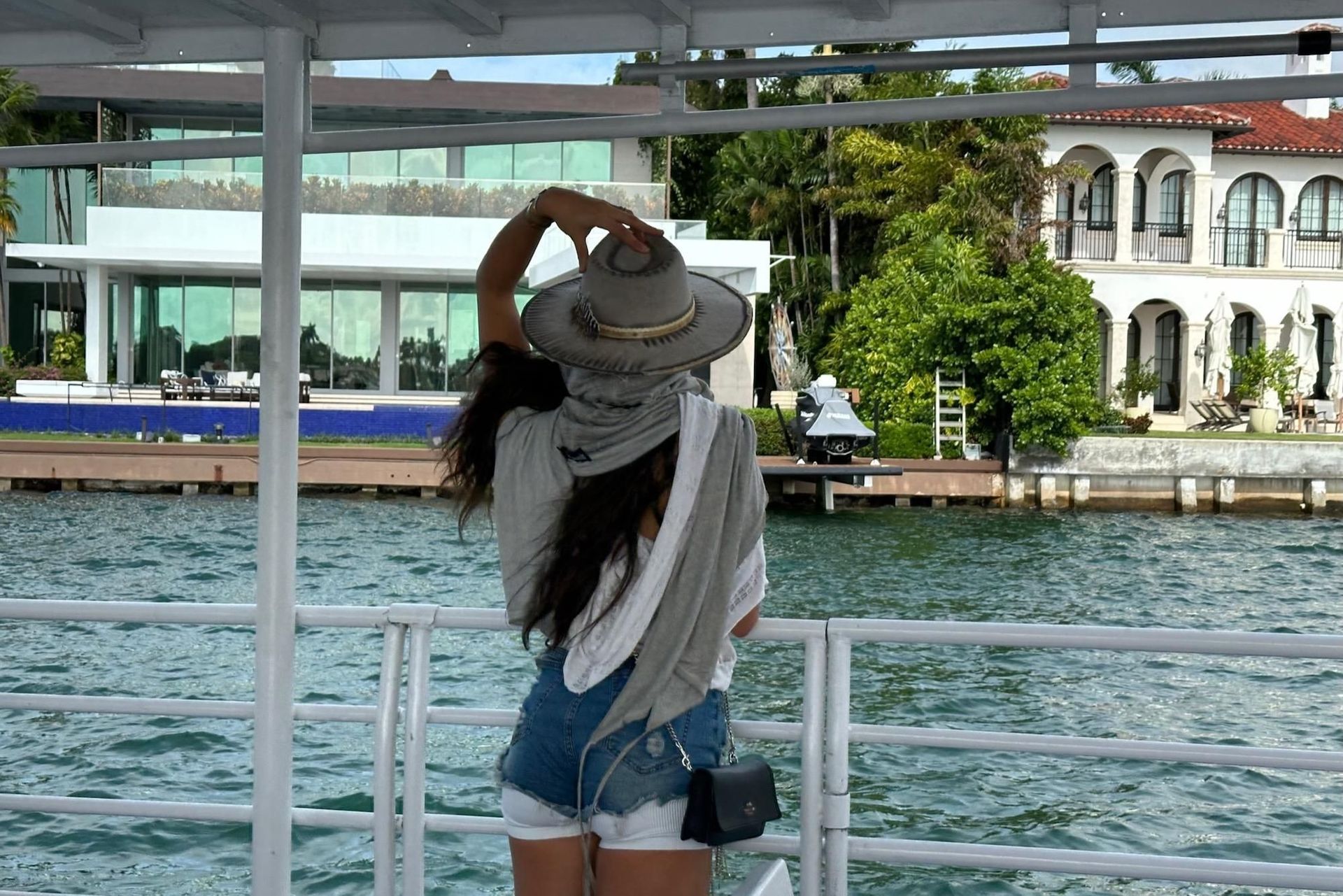 Woman on boat, wearing hat, looking at waterfront houses.