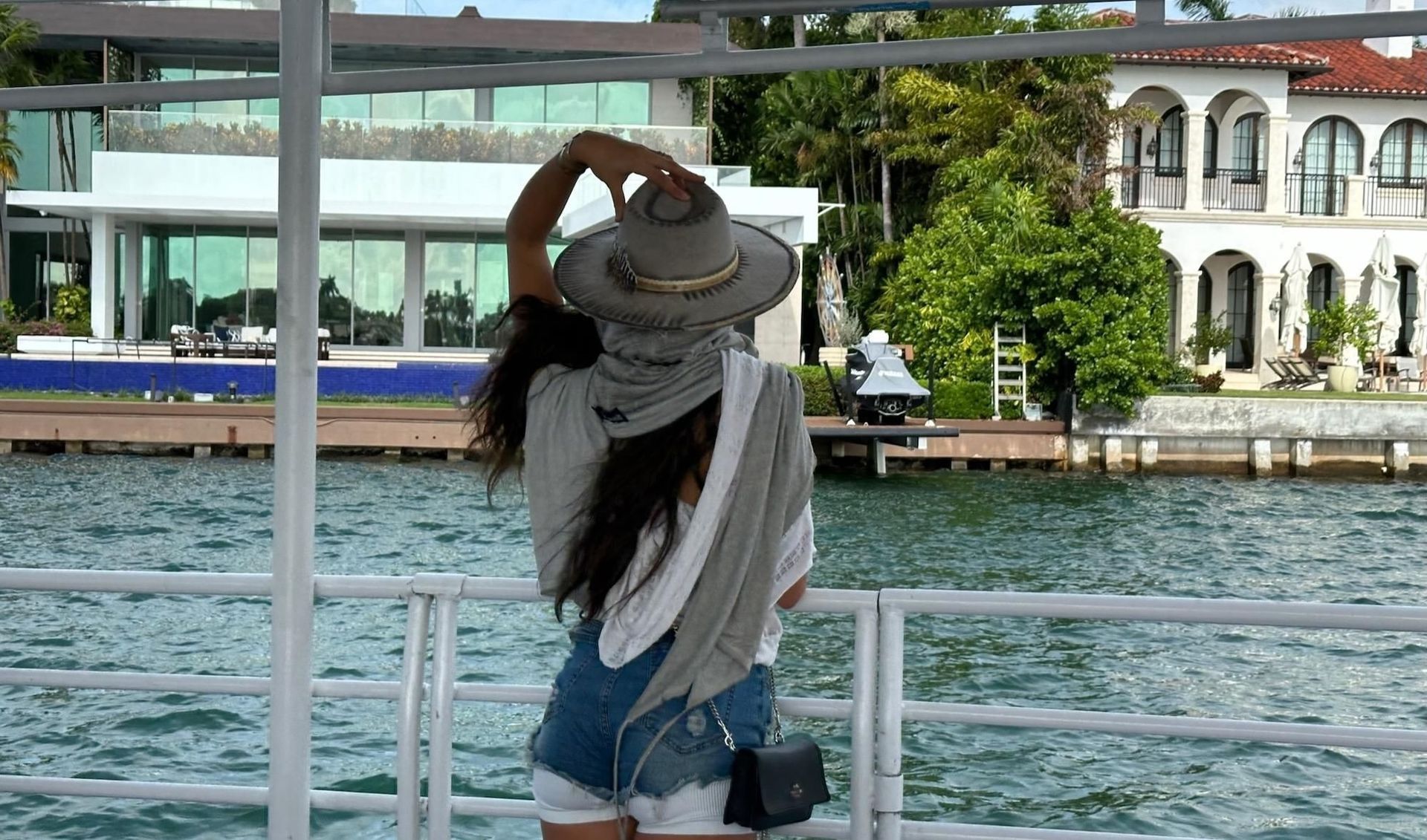Woman on a boat adjusting hat, looking at waterfront homes.
