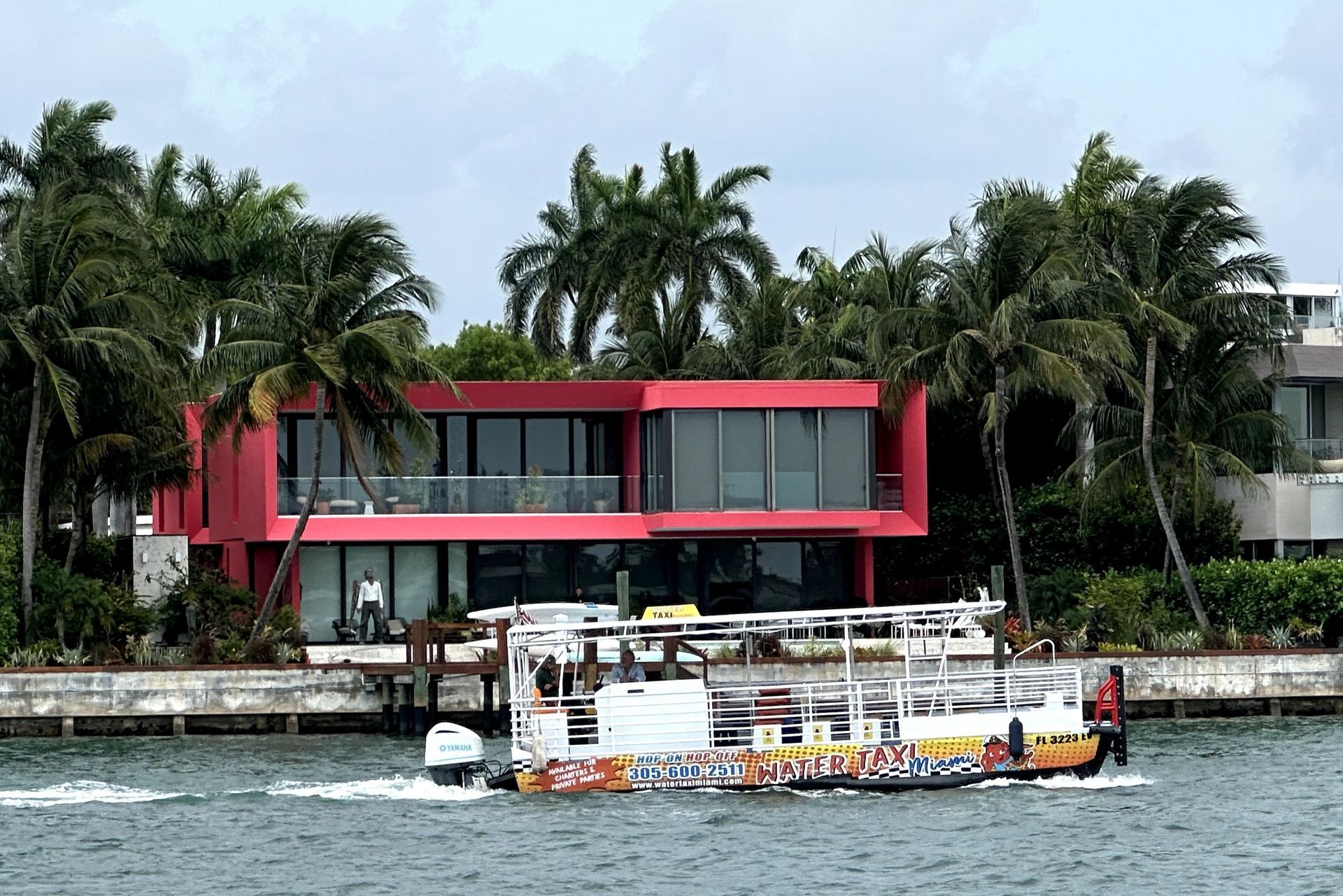 Red modern house with large windows, overlooking water; boat in foreground.
