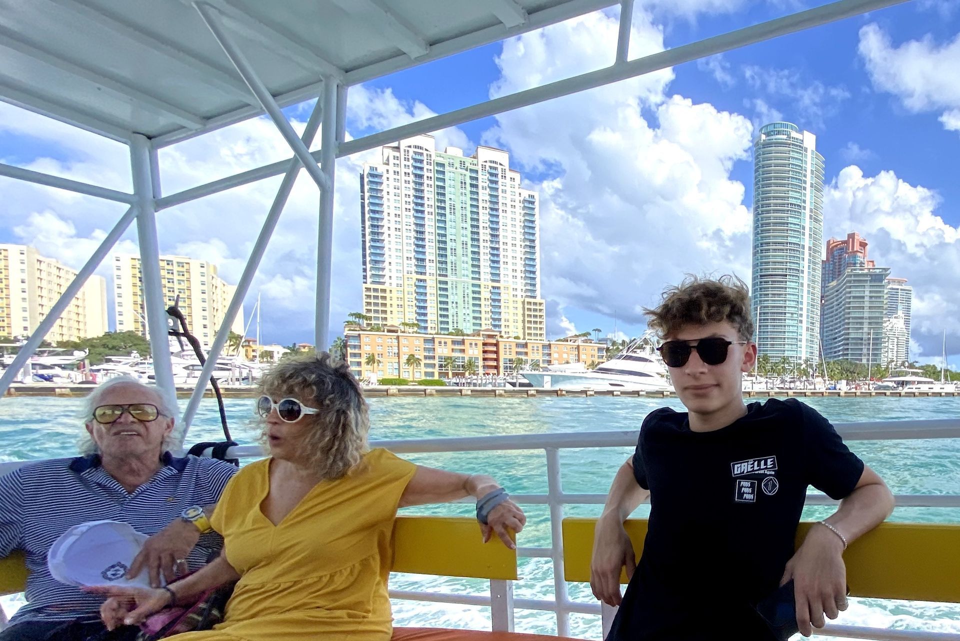 Three people on a boat with city buildings in the background. Sunny day.