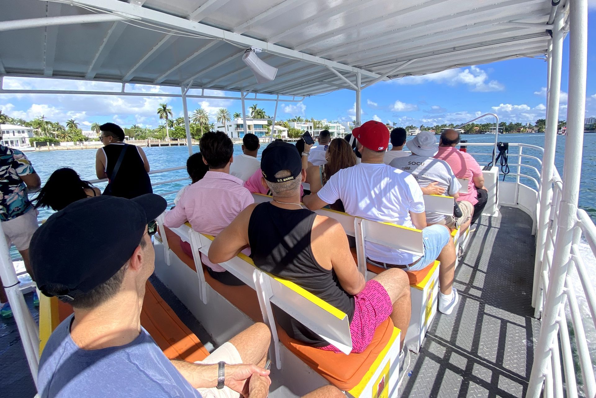 People on a boat ride, traveling on the water. Some are facing forward, some looking at the camera. Sunny day.