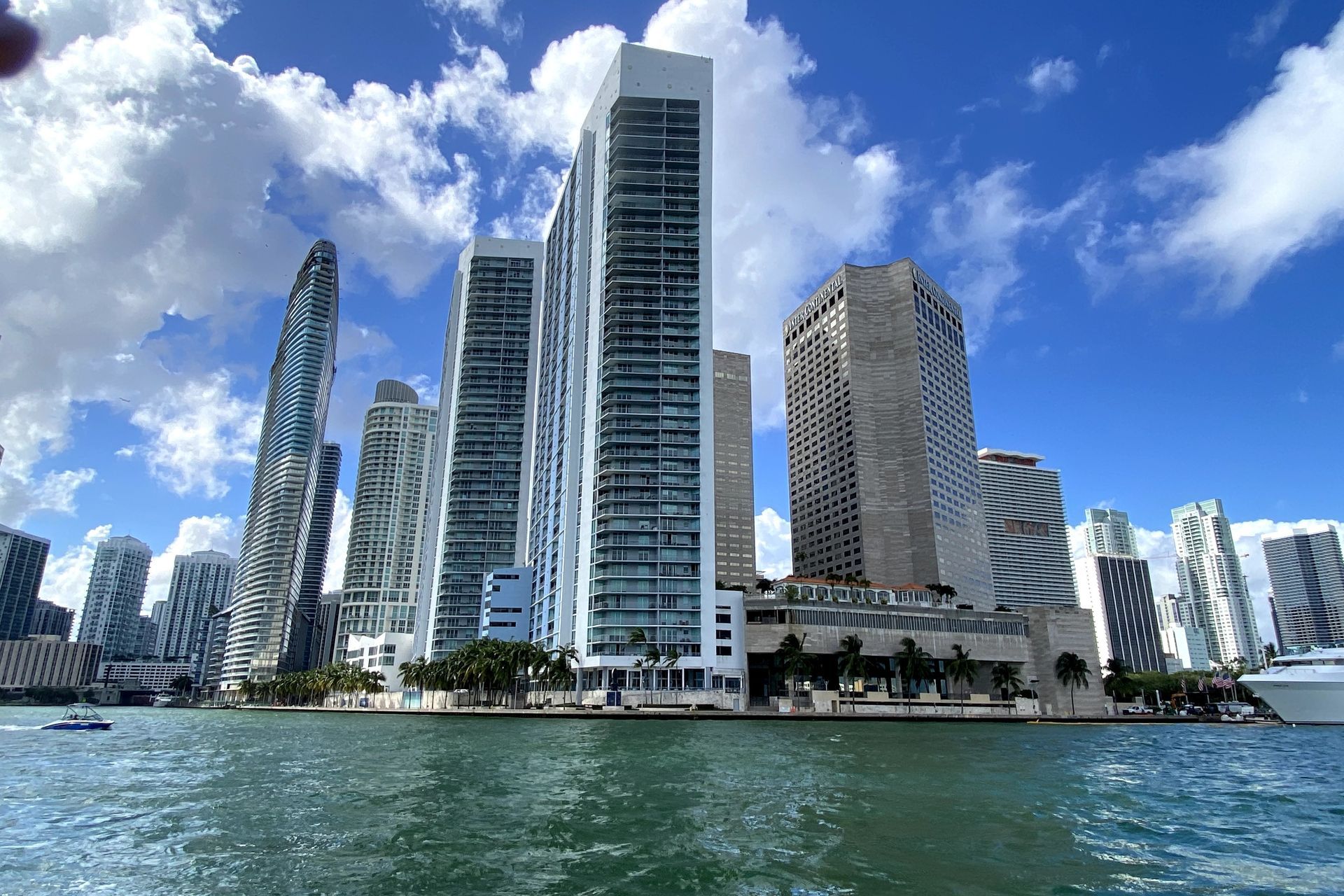 Skyscrapers along a waterfront under a bright blue sky with fluffy white clouds, Miami.