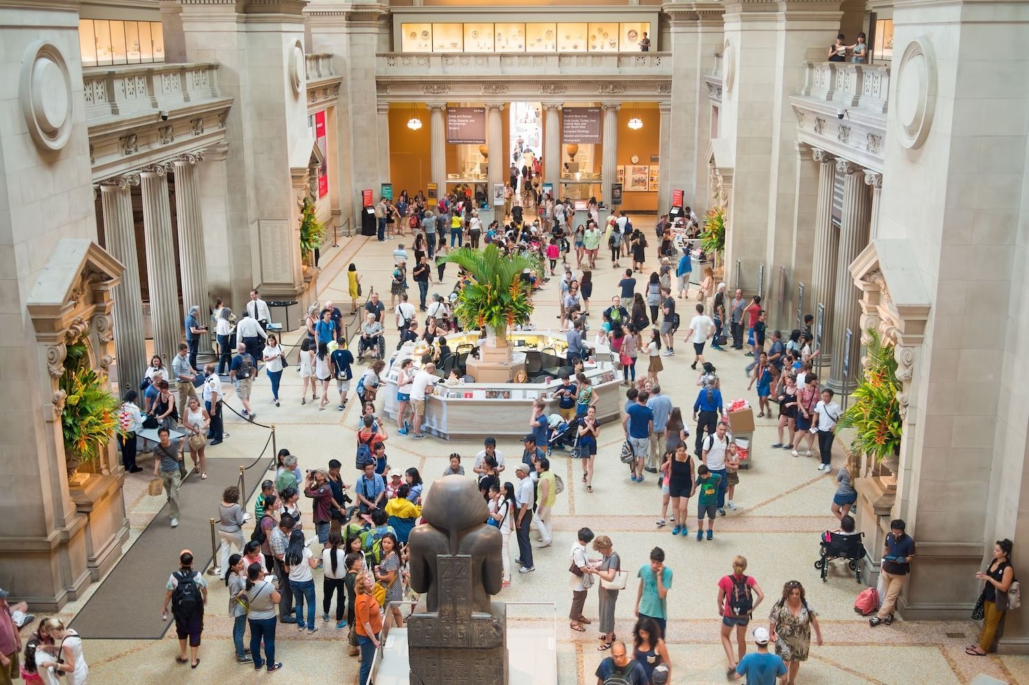 A crowded museum lobby with many visitors milling about, seen from an elevated vantage point.