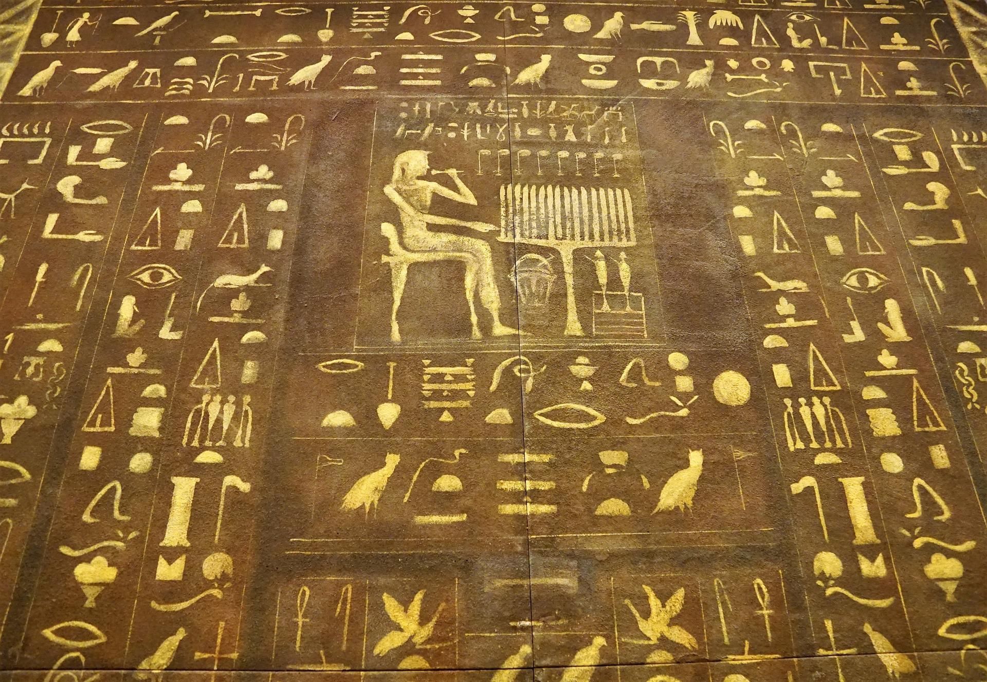 Ancient Egyptian hieroglyphs and seated figure playing a stringed instrument, brown with gold details.