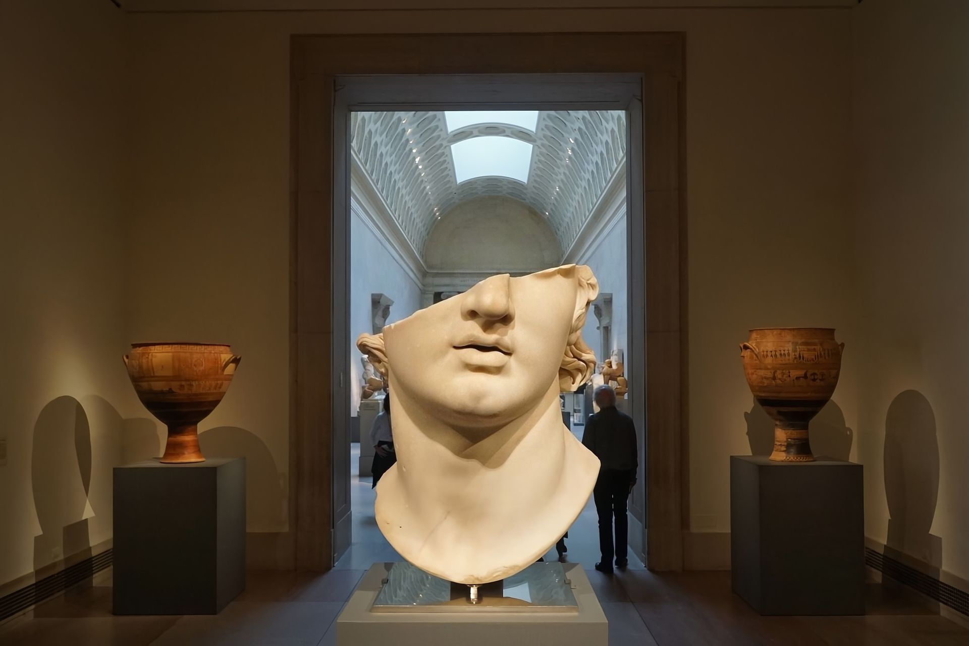 Marble sculpture head in museum hall with pottery on each side.
