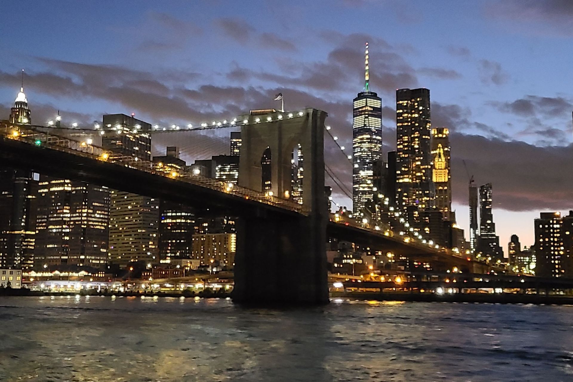 Brooklyn Bridge at dusk with illuminated Manhattan skyline.
