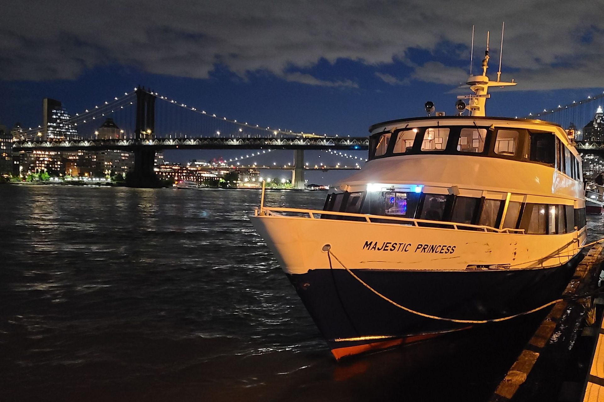 A boat docked at night with a bridge and city skyline in the background.