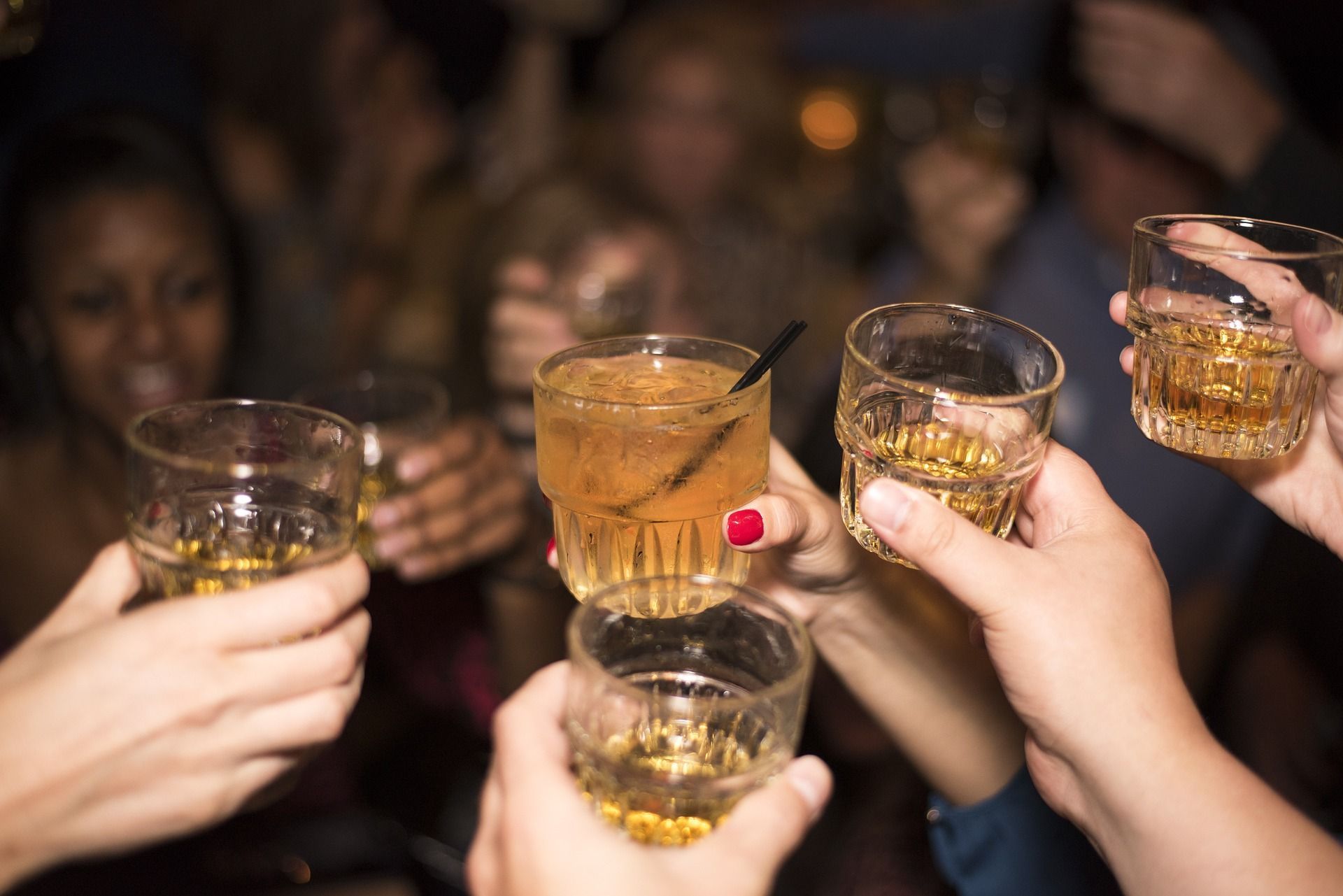People in a bar, toasting with whiskey glasses. Focus on hands holding glasses in the air.