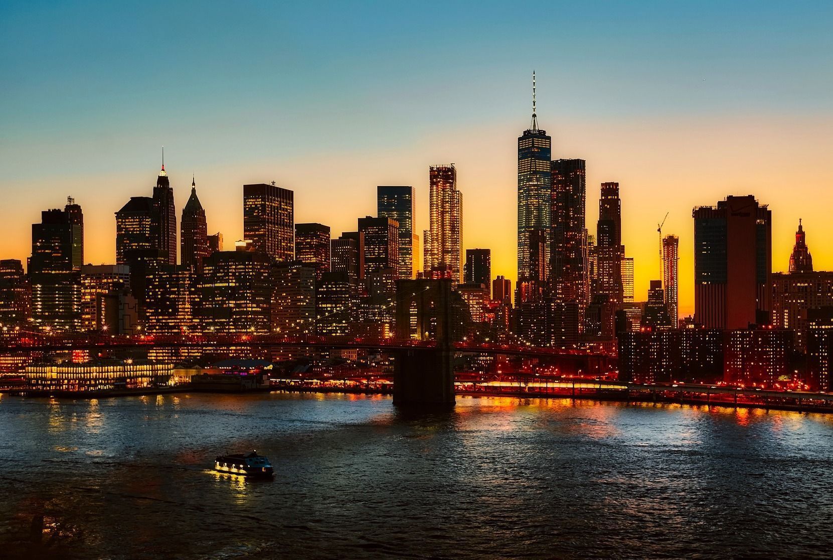 New York City skyline at dusk, buildings silhouetted against an orange and blue sky over the water.