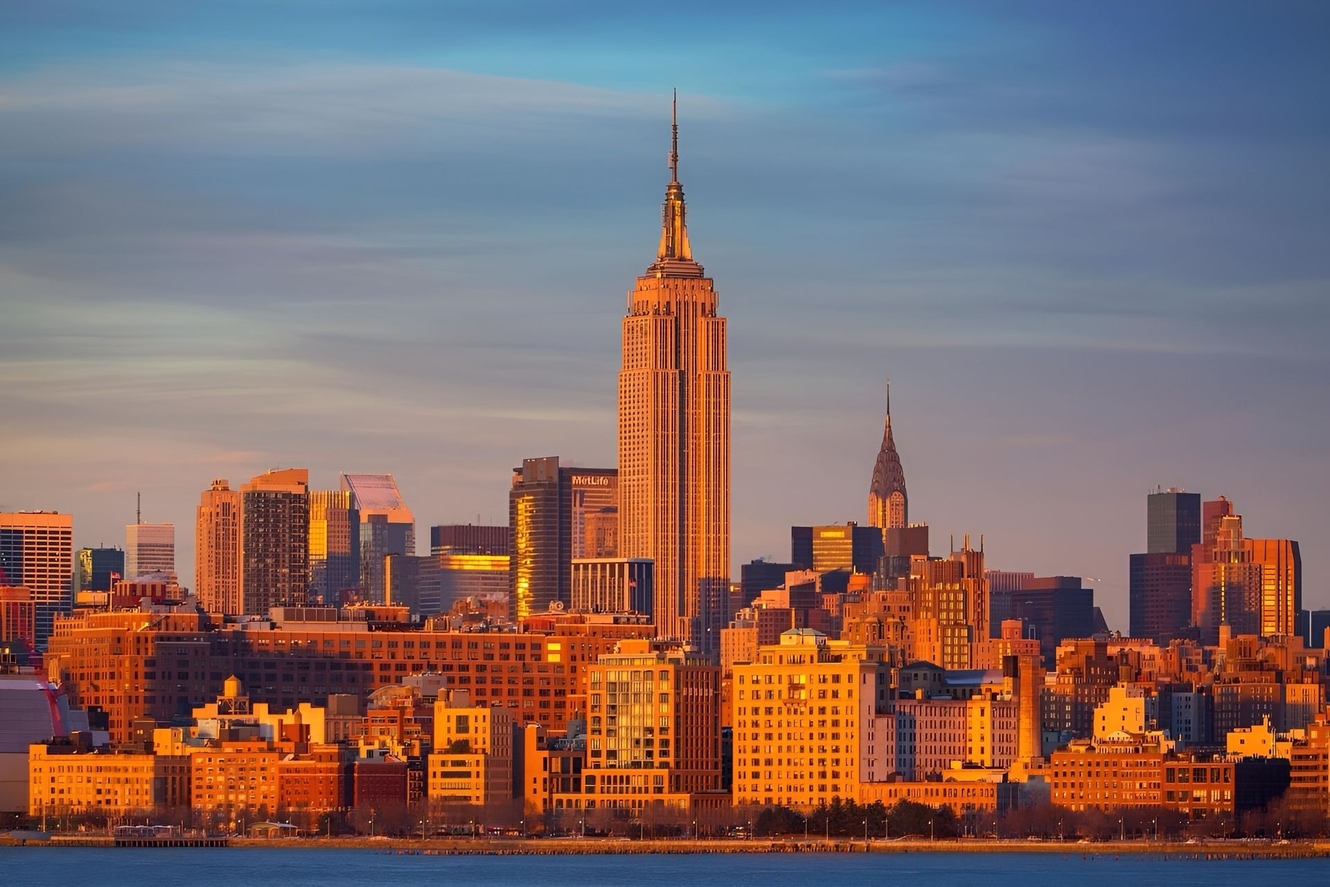 New York City skyline at sunrise, Empire State Building prominent in golden light.