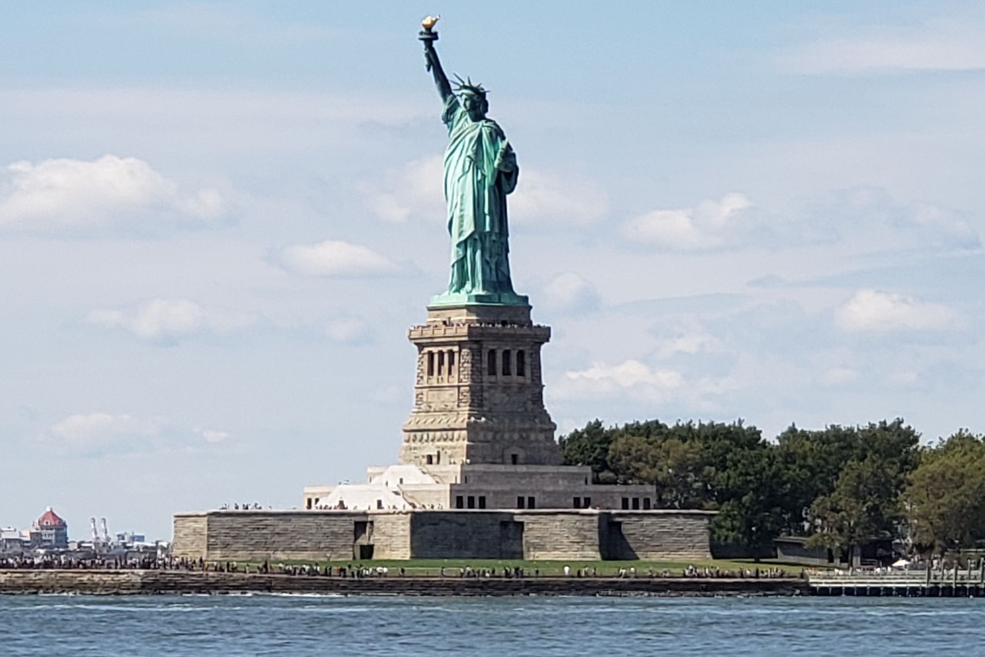 Statue of Liberty, New York City, standing tall with arm raised, torch held high, blue sky background.