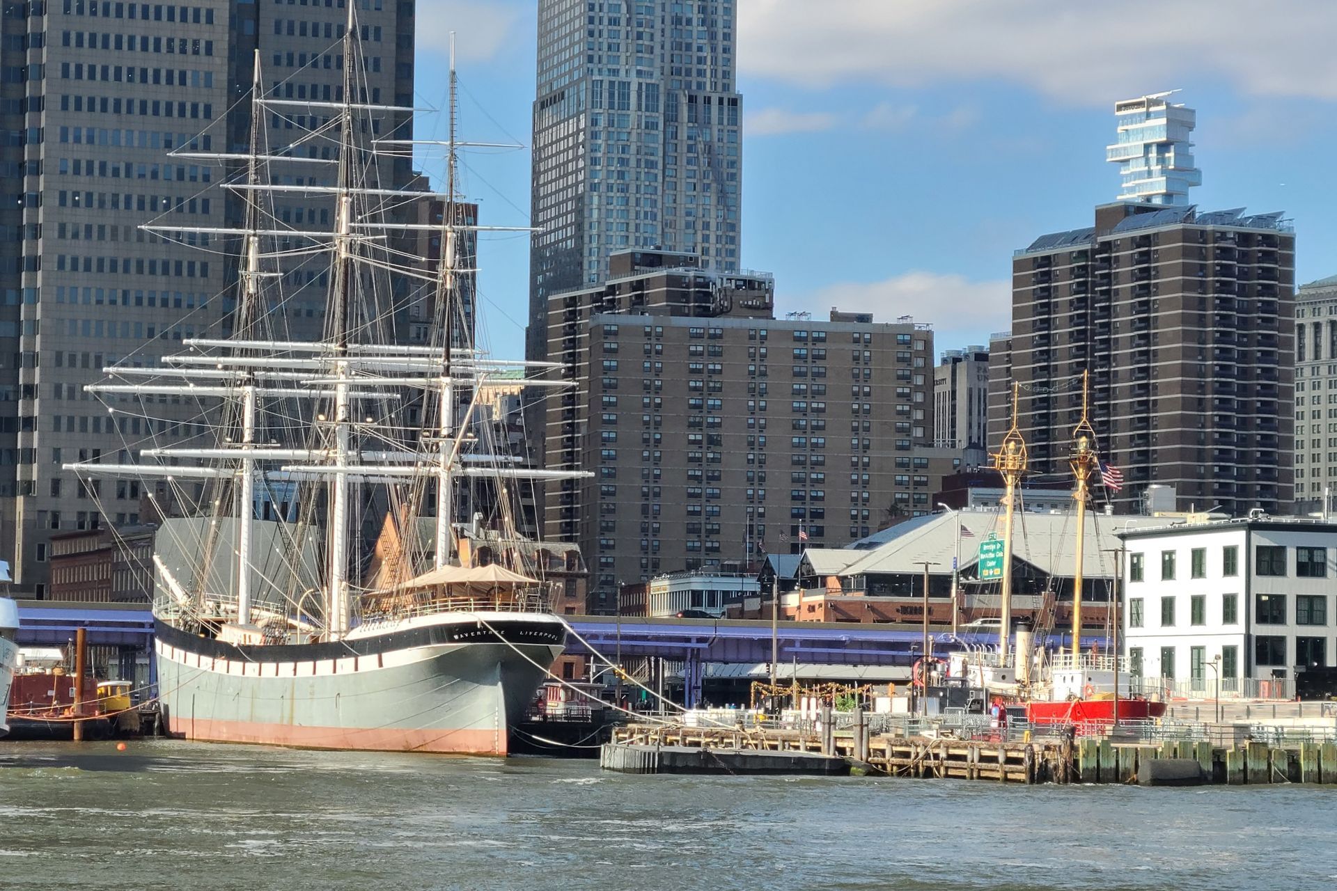 Tall ship docked in harbor, skyline with skyscrapers in background.