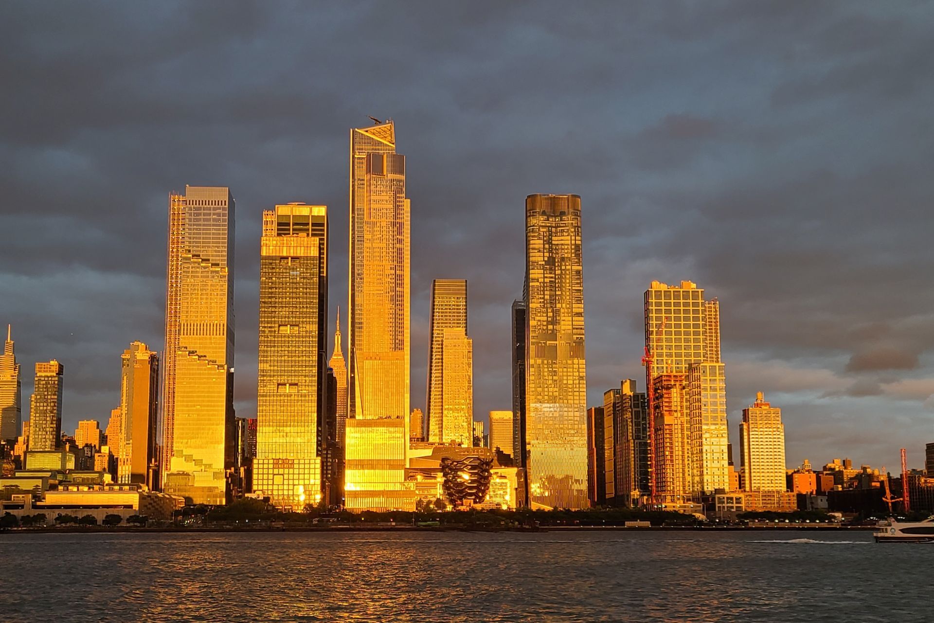 Golden sunset illuminates Manhattan skyscrapers over water.