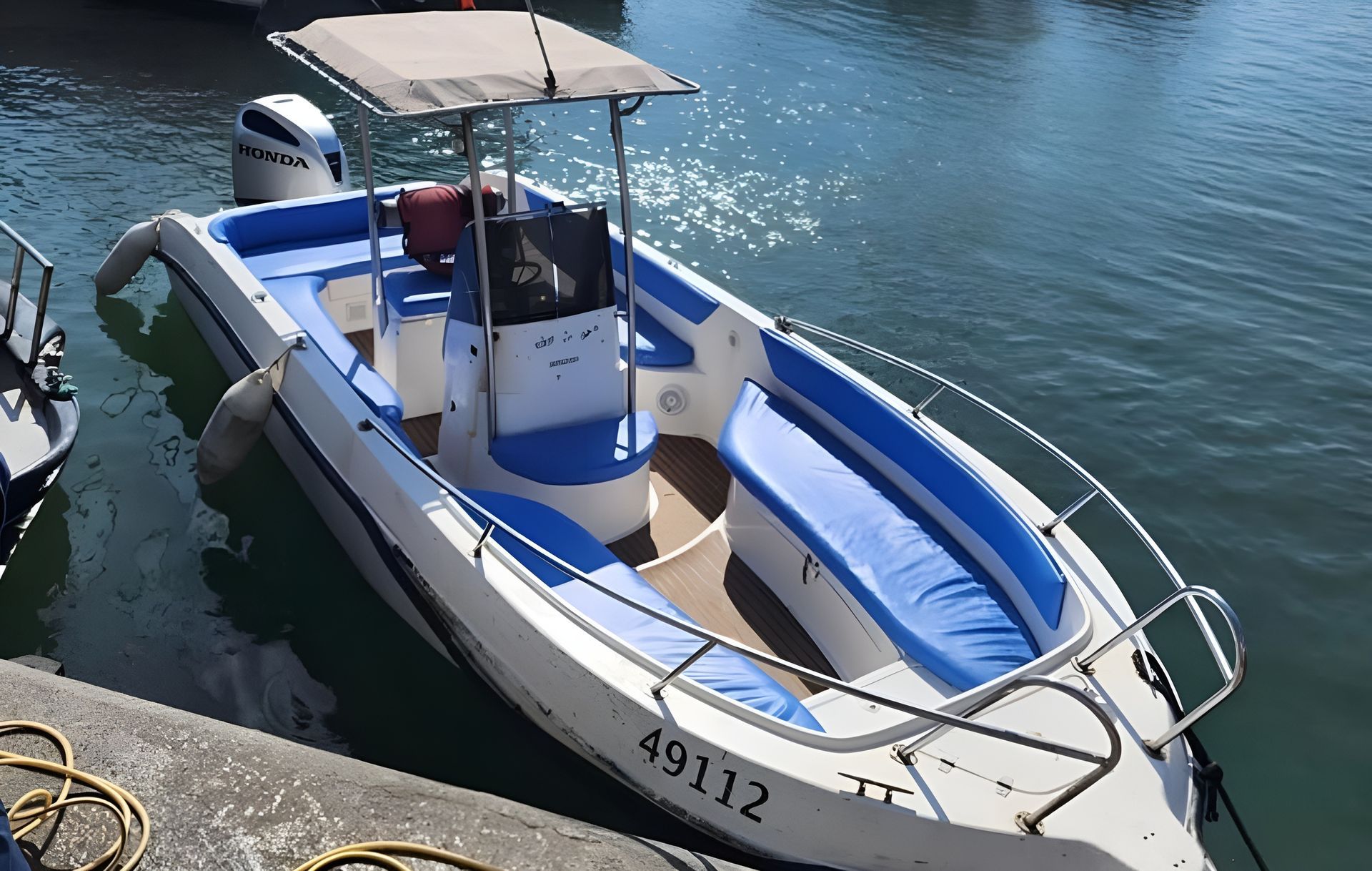 White and blue motorboat with a canopy docked near a pier.