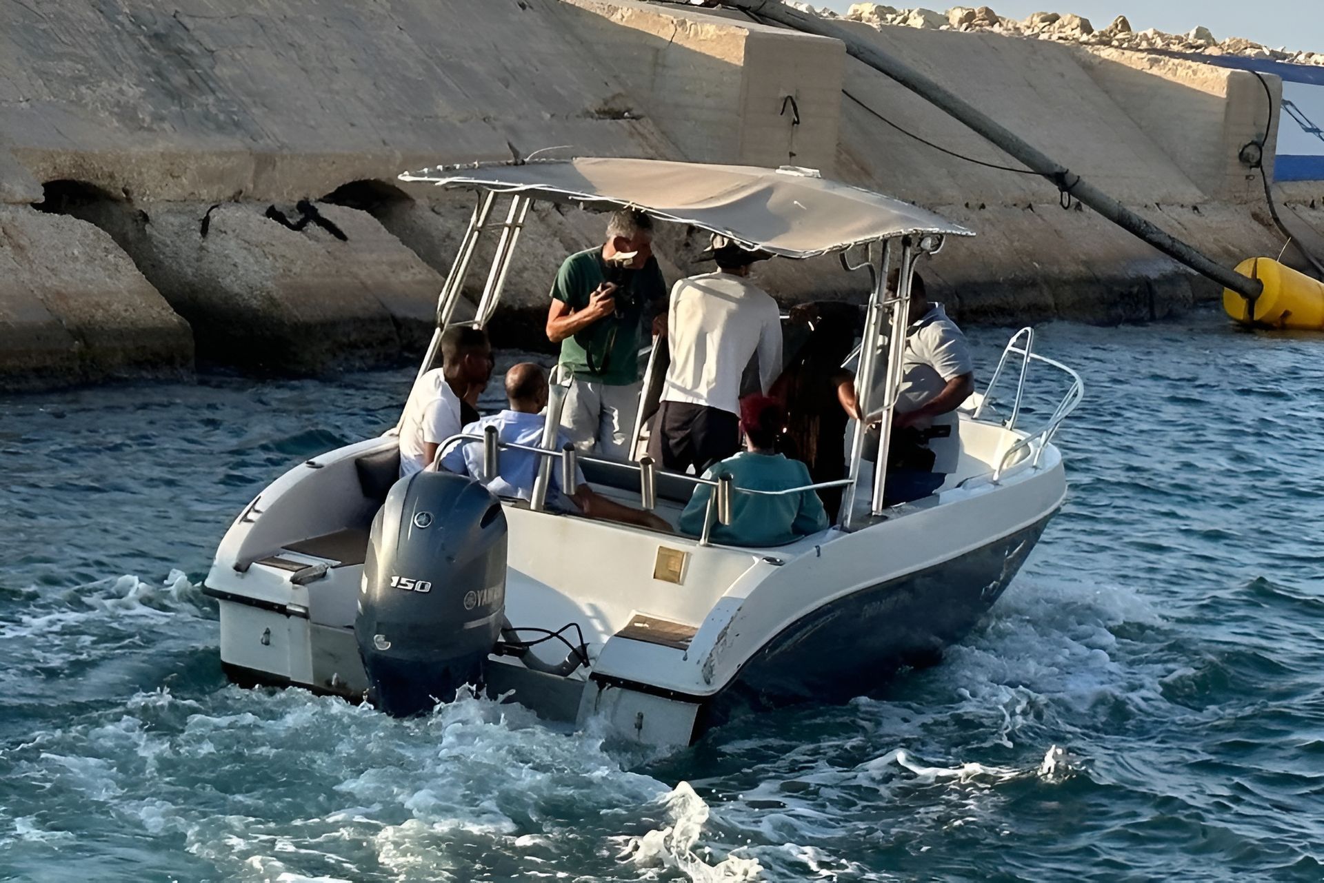 Boat with several people near a concrete structure. People are on board in various attire.