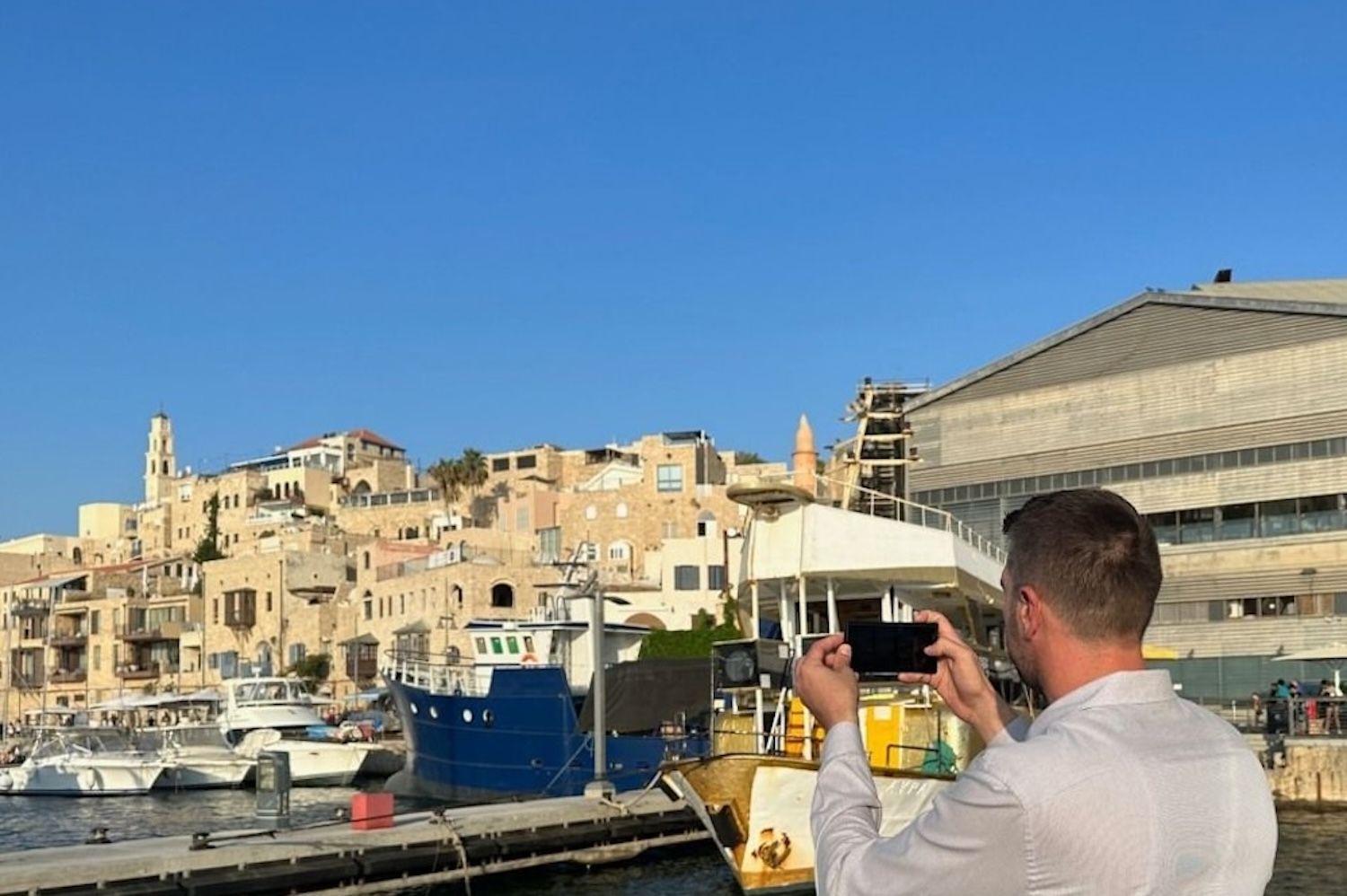 Man taking a photo of the old city and boats on a sunny day at a harbor.