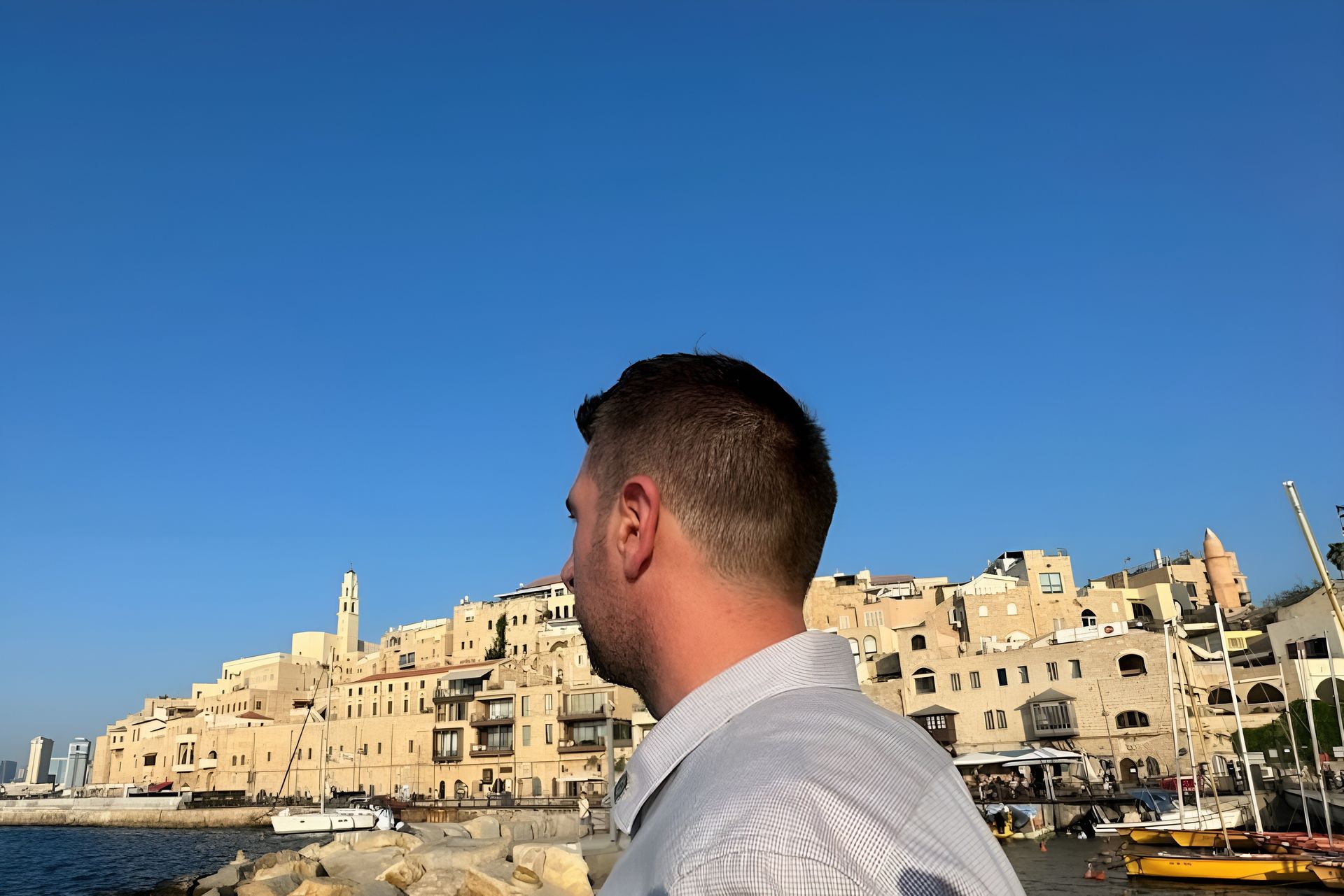 Man looking at the historic Jaffa port and city in Israel under a clear blue sky.
