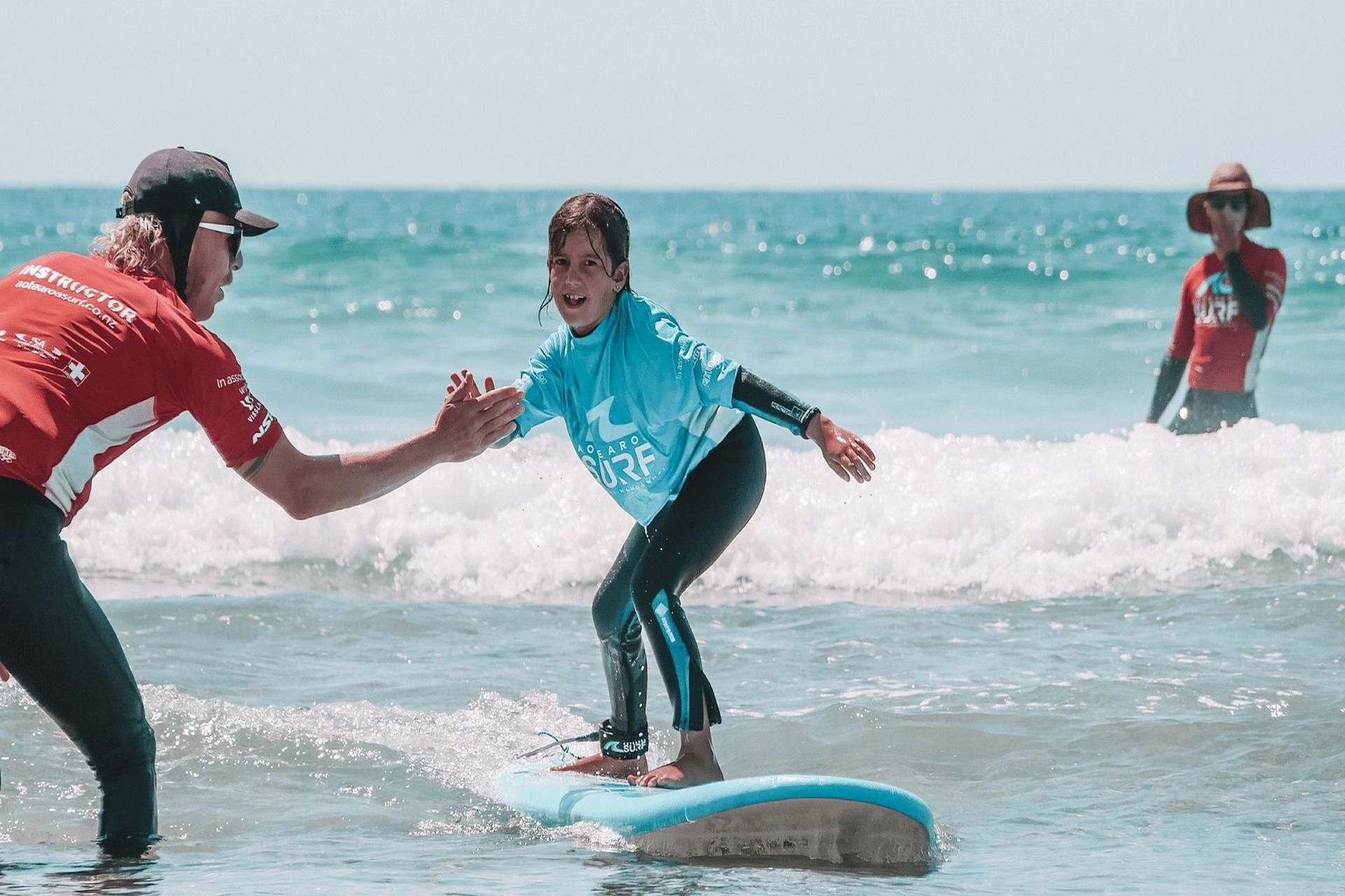 A kid receiving surfing lessons, holding the hand of the instructor as he catches a wave.
