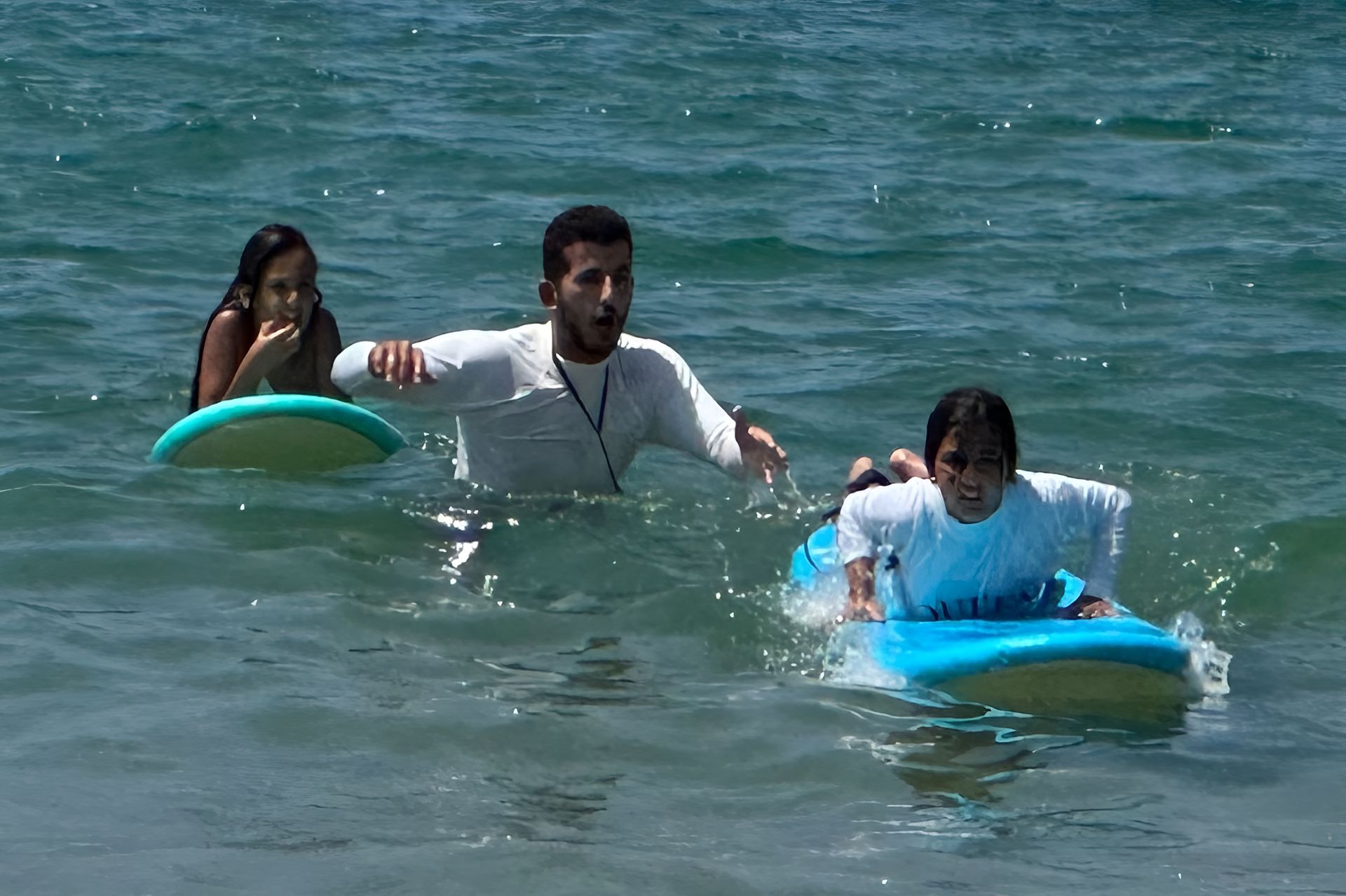 Man teaching two children to surf in the ocean.