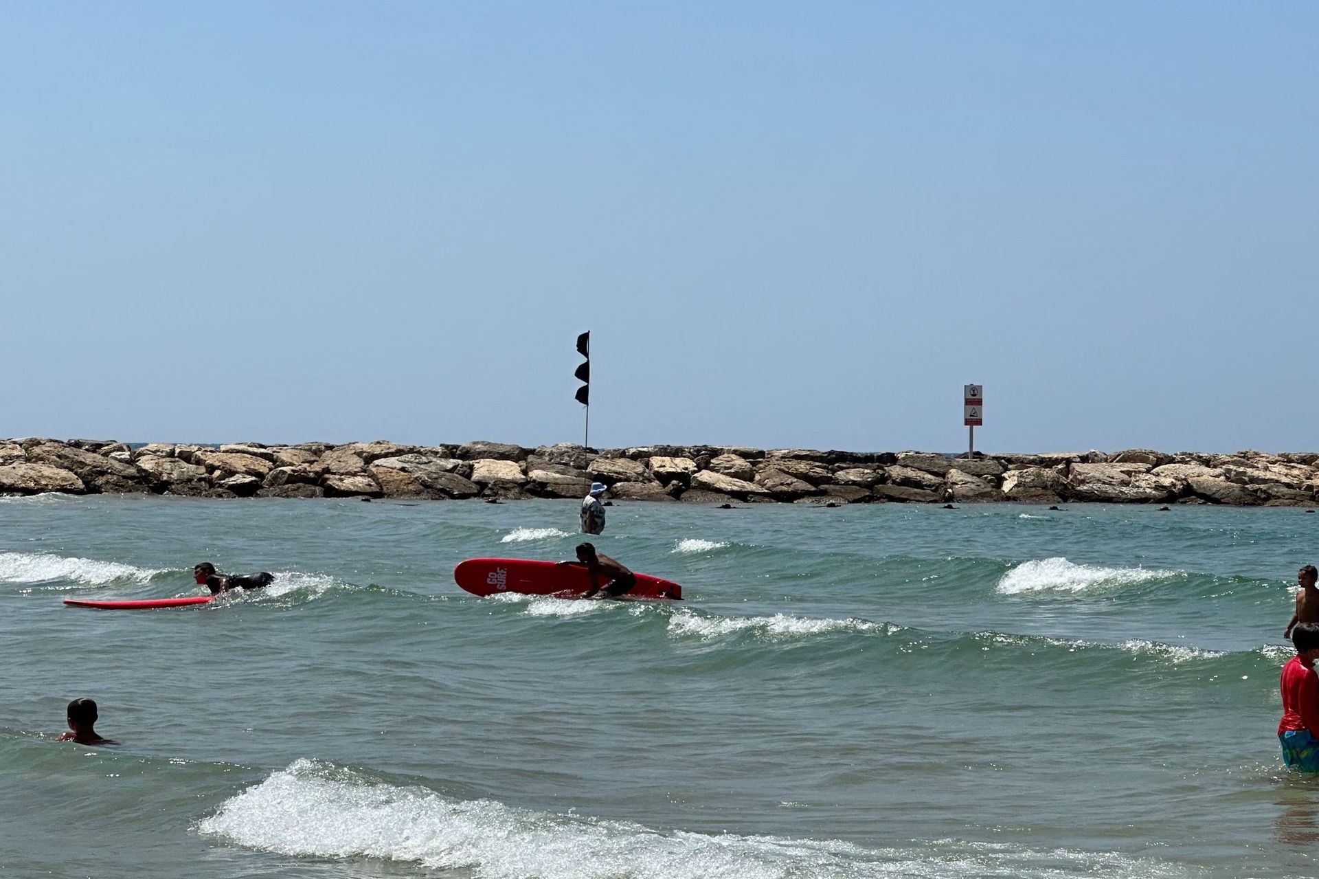 People swimming and surfing at a beach with a stone wall.