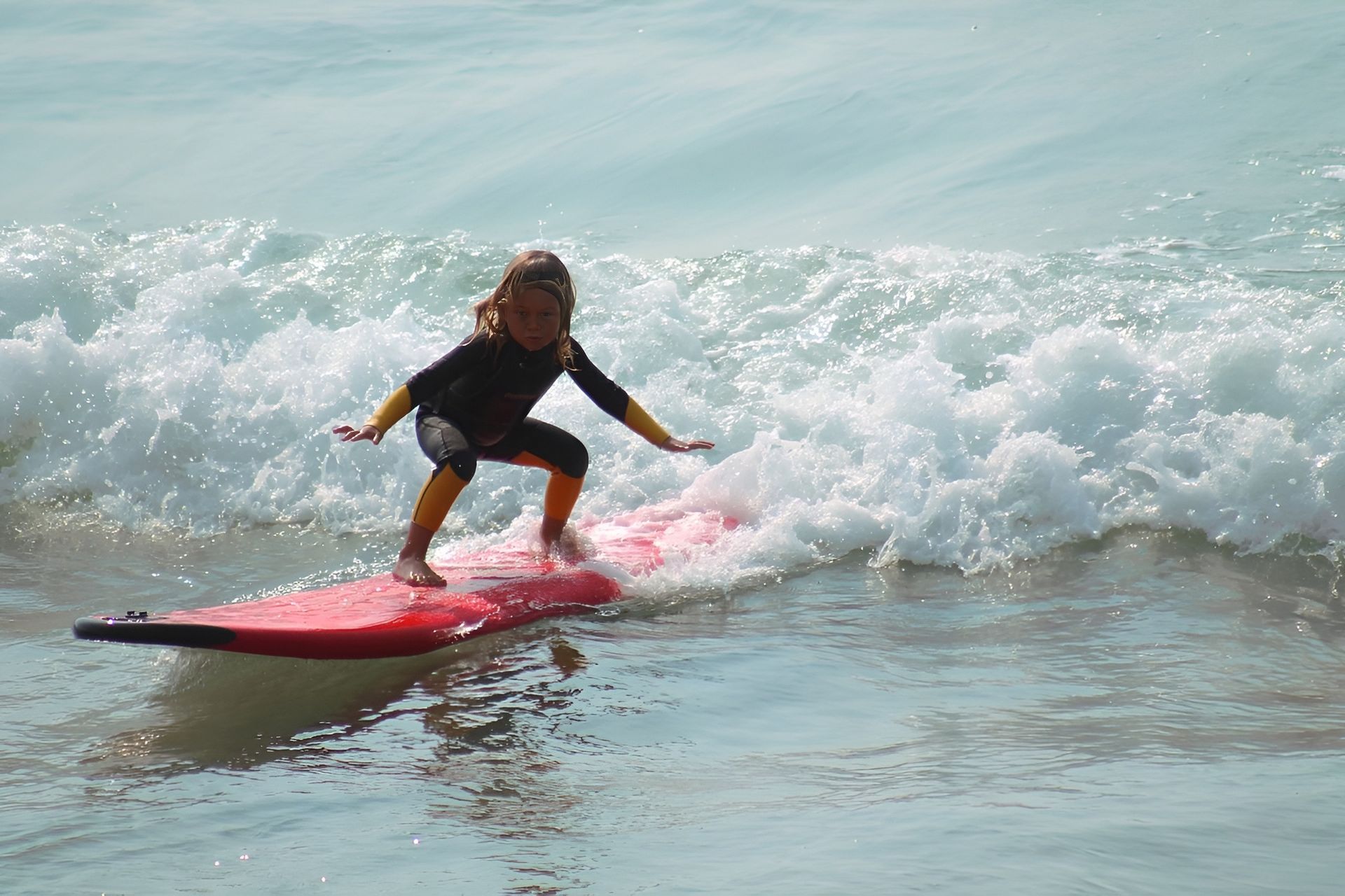 Girl surfing a wave on a red board in the ocean, wearing a wetsuit.