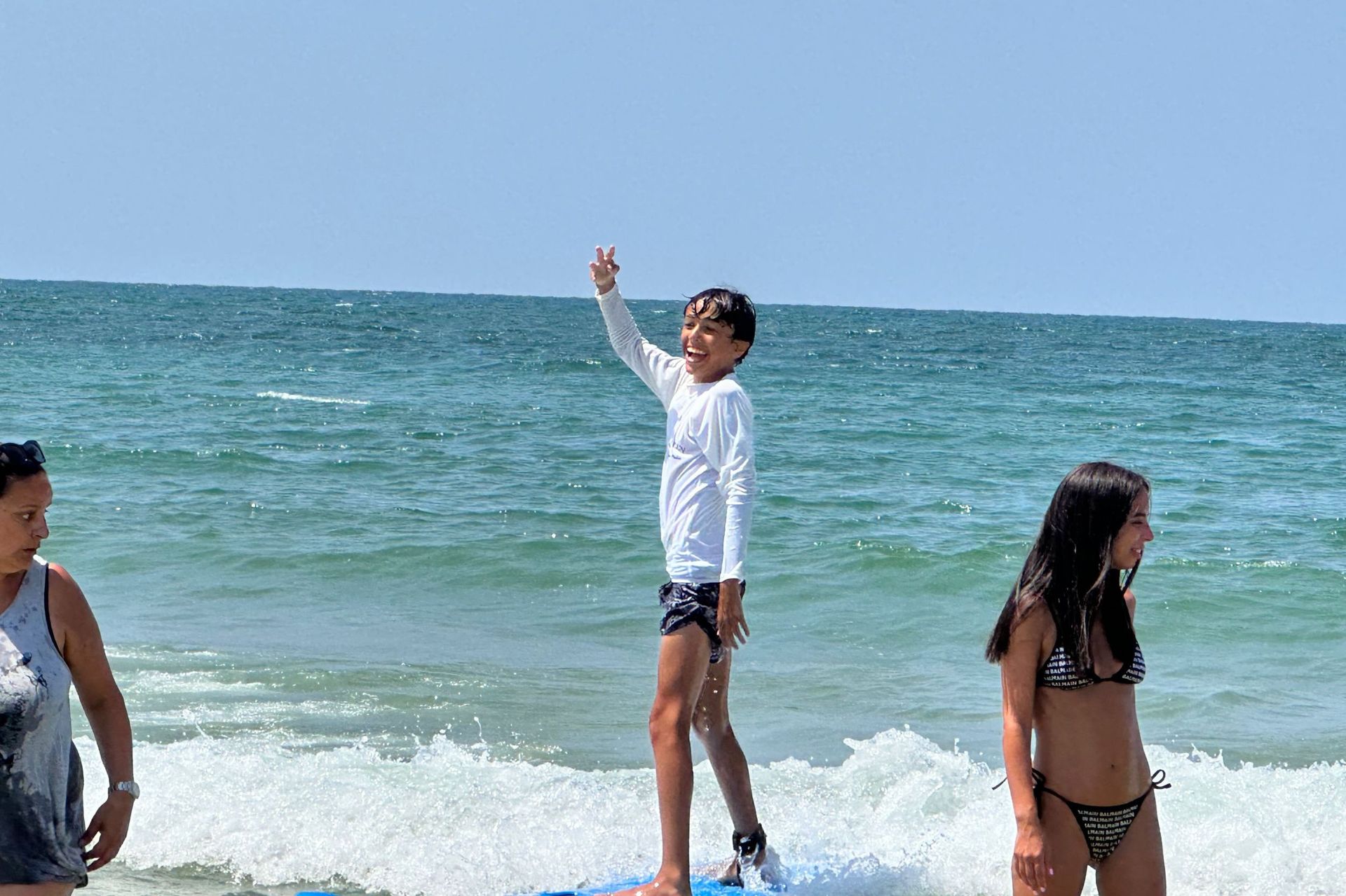 Boy on boogie board waves, waving arm. Other people in surf at beach.
