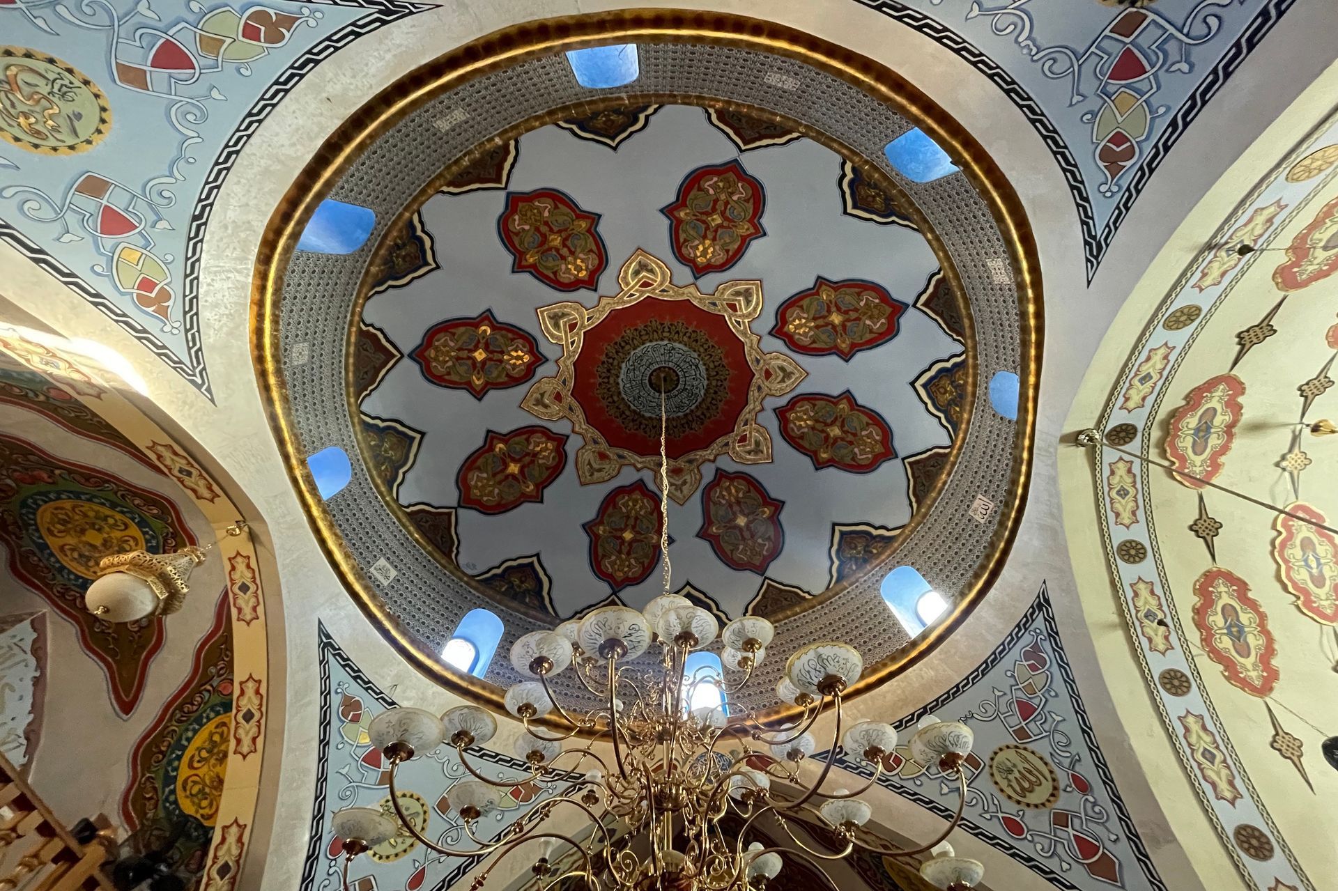 Ornate mosque ceiling with a gold and floral design, featuring a central dome and a chandelier.