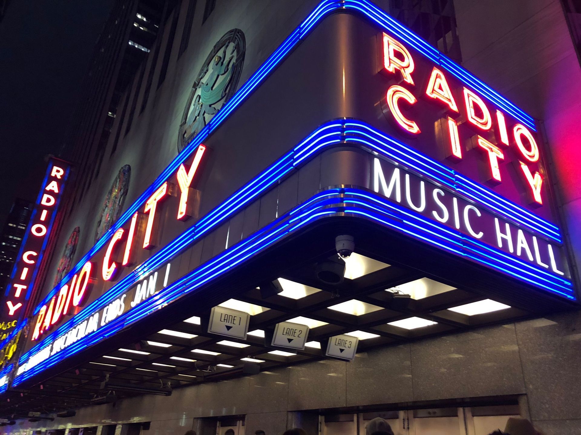 Radio City Music Hall exterior, neon sign in bright blue and red, night time.