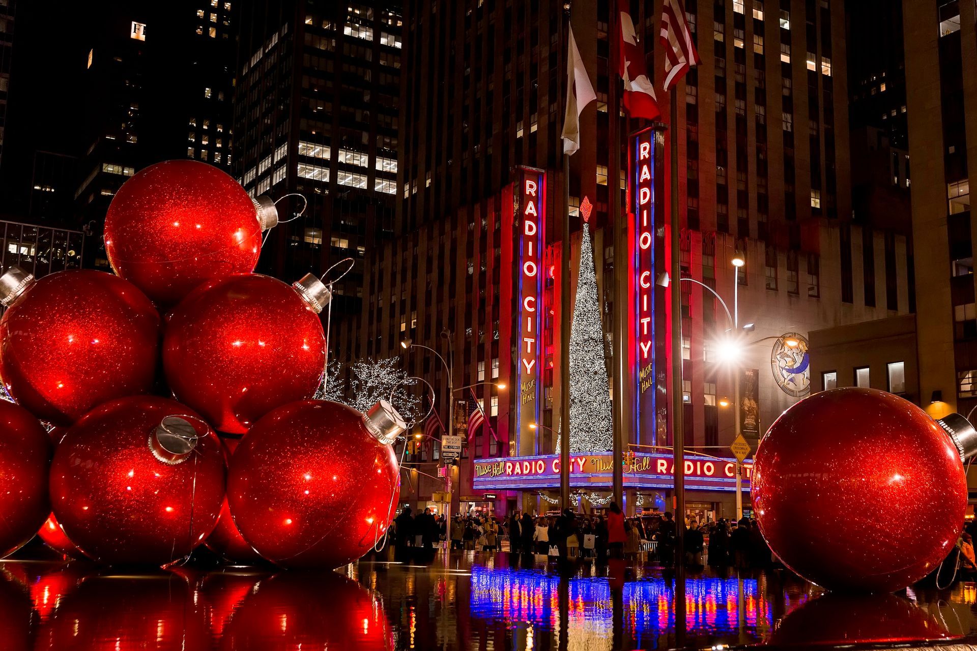 Giant red Christmas ornaments in front of Radio City Music Hall, New York City, at night.