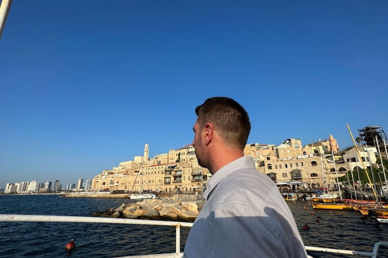 Man on boat looking at buildings on the coast under a blue sky.