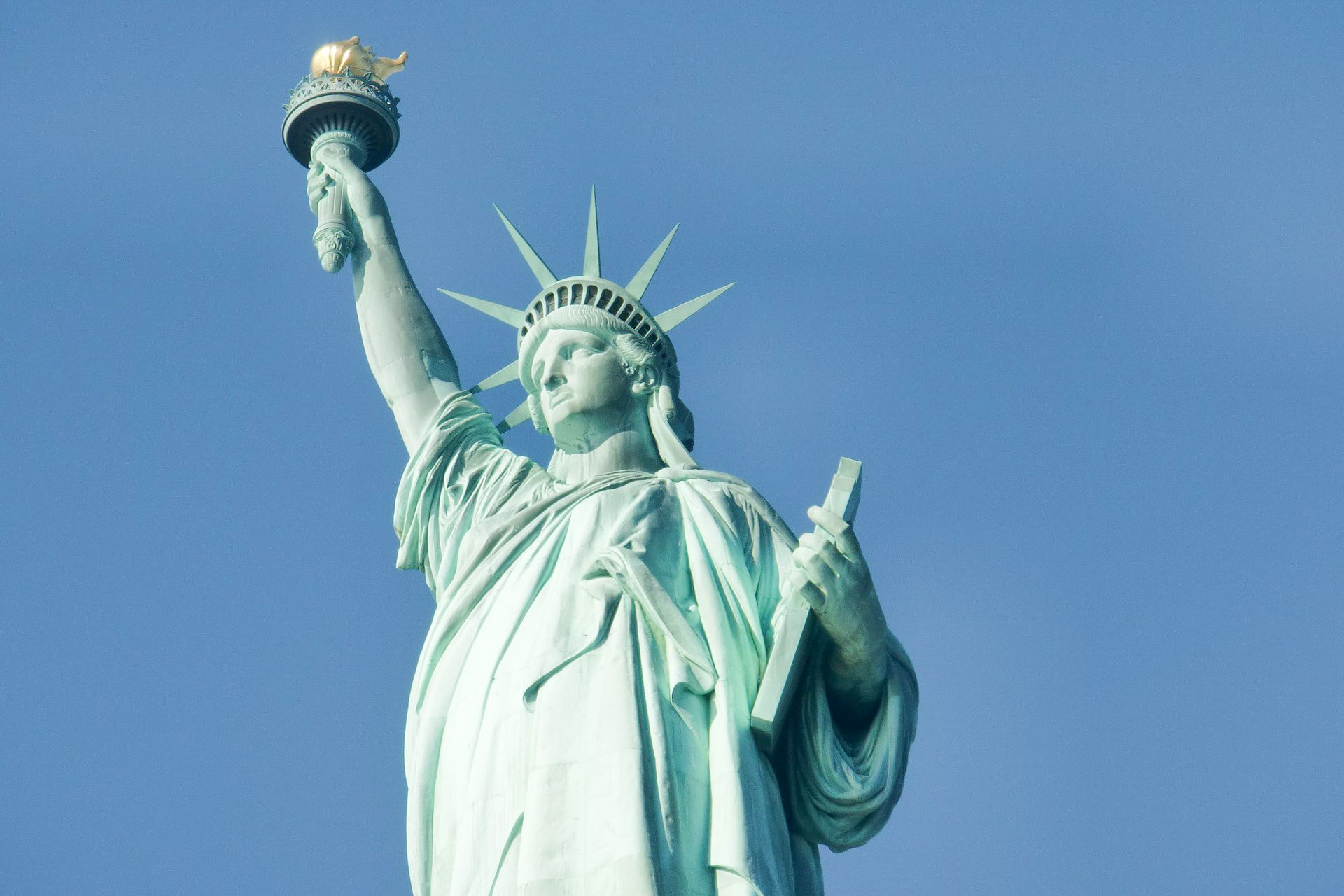 Statue of Liberty, holding torch, against clear blue sky.