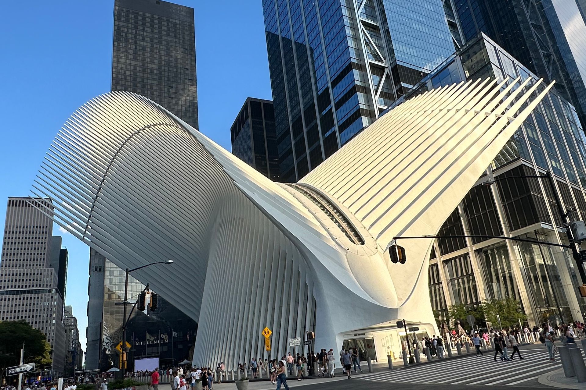 White, wing-like Oculus building amidst tall skyscrapers in New York City. People are walking nearby.